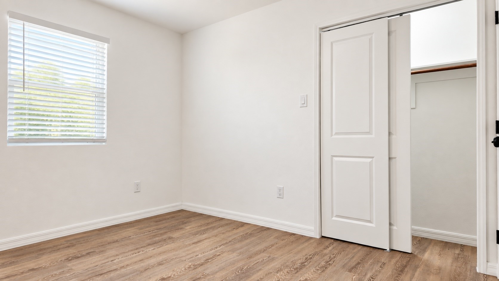 Vacant bedroom with wood floors, a window with blinds, and an open closet.