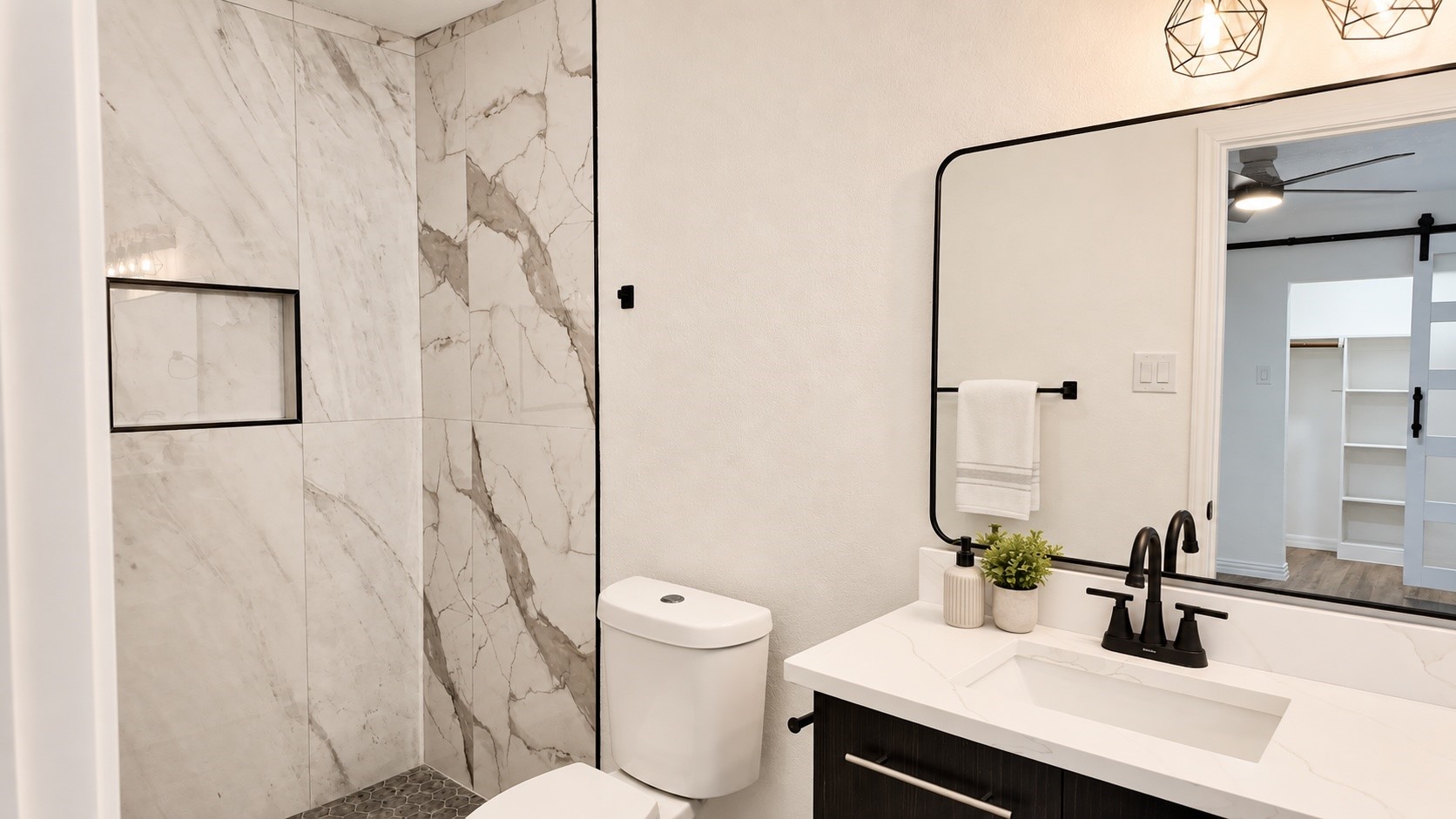 Renovated bathroom with marble-look shower tile, dark hexagonal floor, and white vanity with black fixtures.