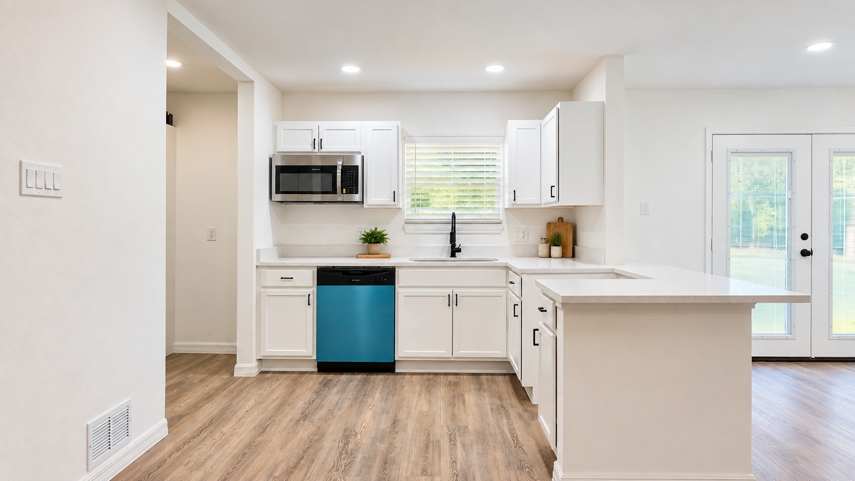 Bright kitchen with white cabinets, a peninsula island, blue dishwasher, and wood-look flooring.
