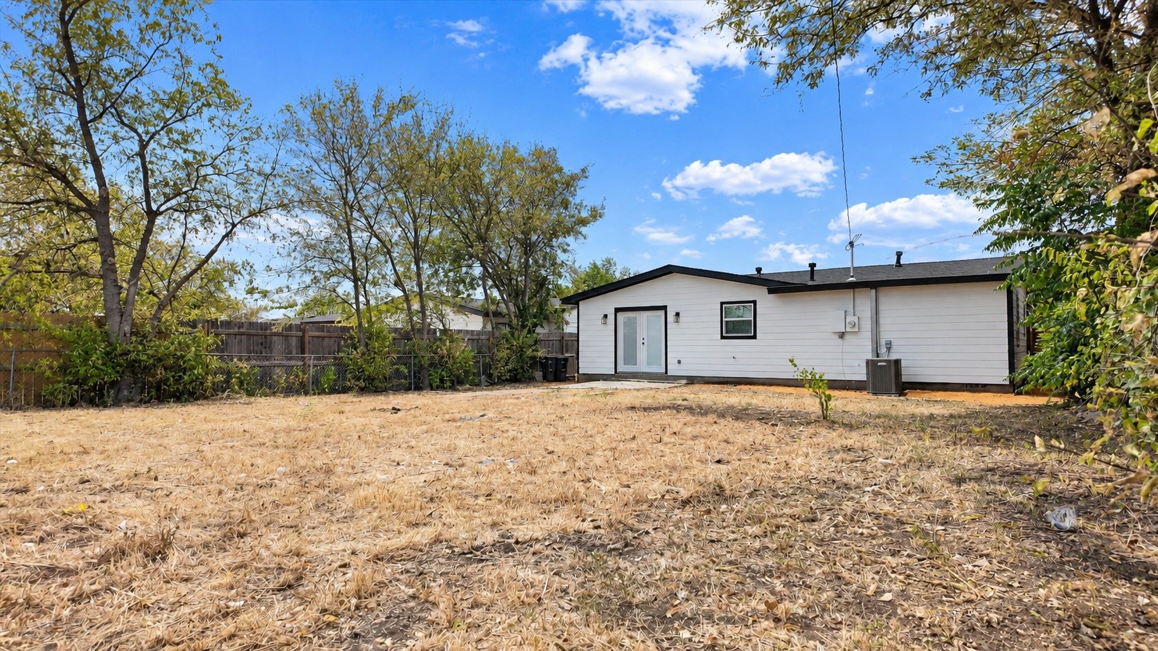 Rear of a white single-story house with black trim and a broad fenced backyard.