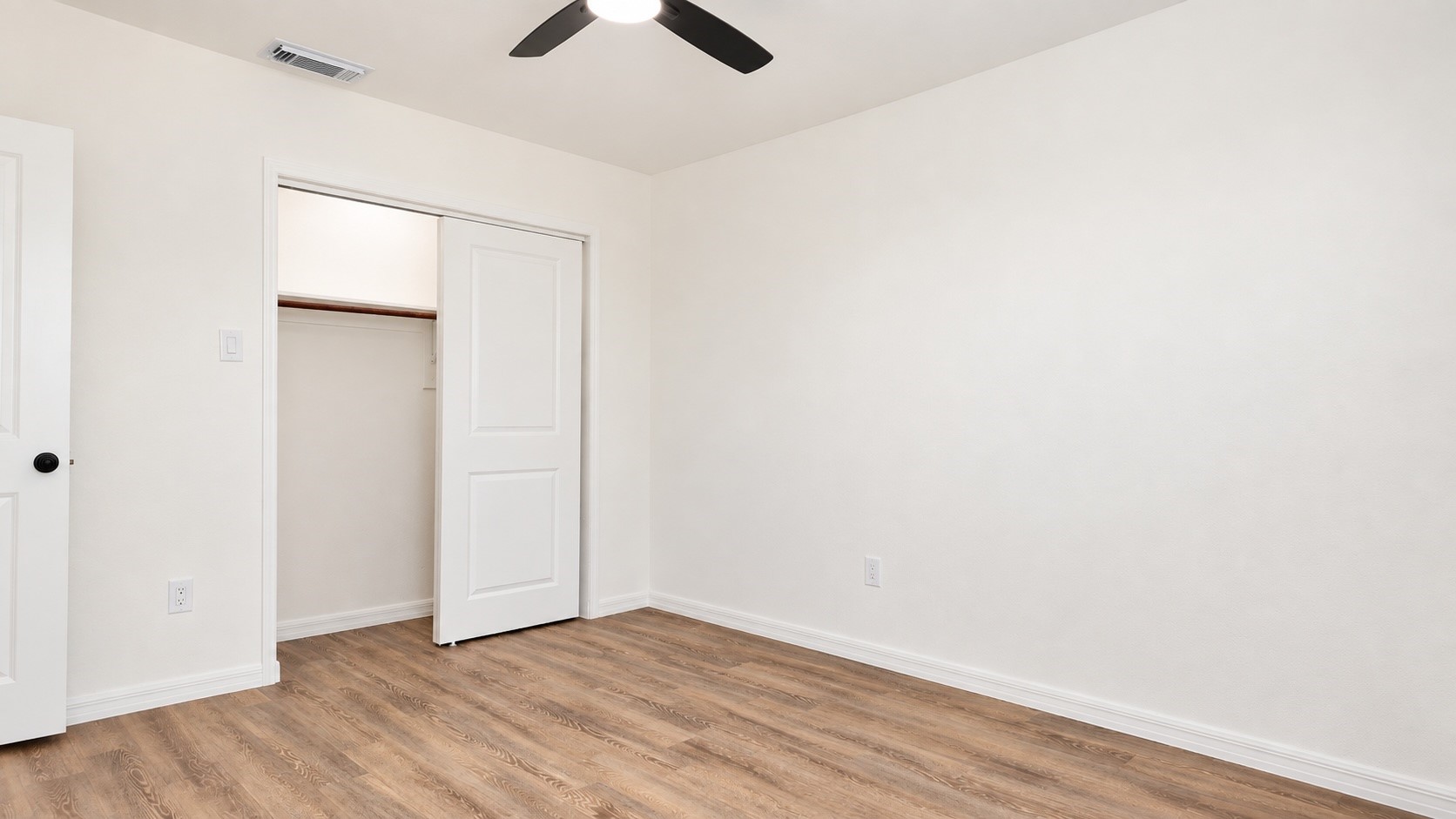 Empty bedroom with wood-look flooring, ceiling fan, and open closet.