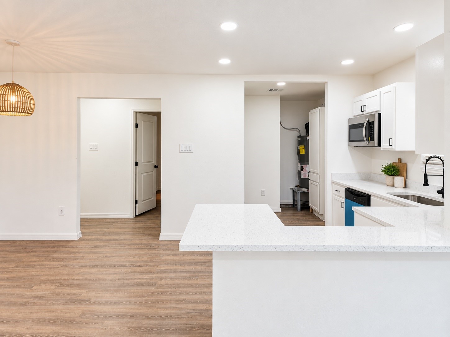 Bright kitchen with a large white quartz island, shaker cabinets, and wood-look flooring.