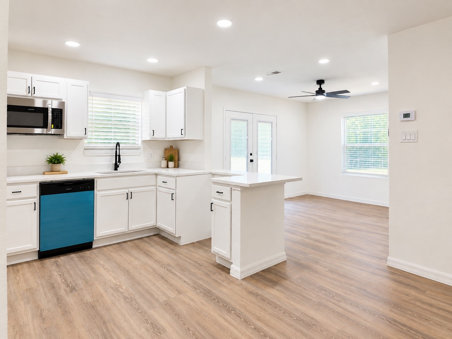 Bright white kitchen with a peninsula, blue-front dishwasher, and wood-look floors opening to a dining area.