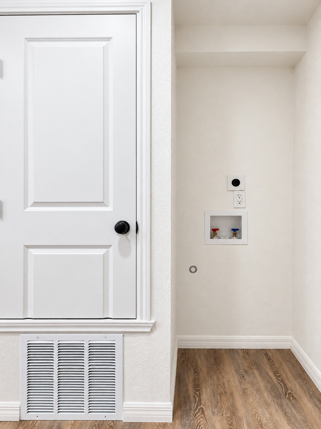 Laundry area with recessed washer and dryer hookups, a white paneled door, and wood-look flooring.