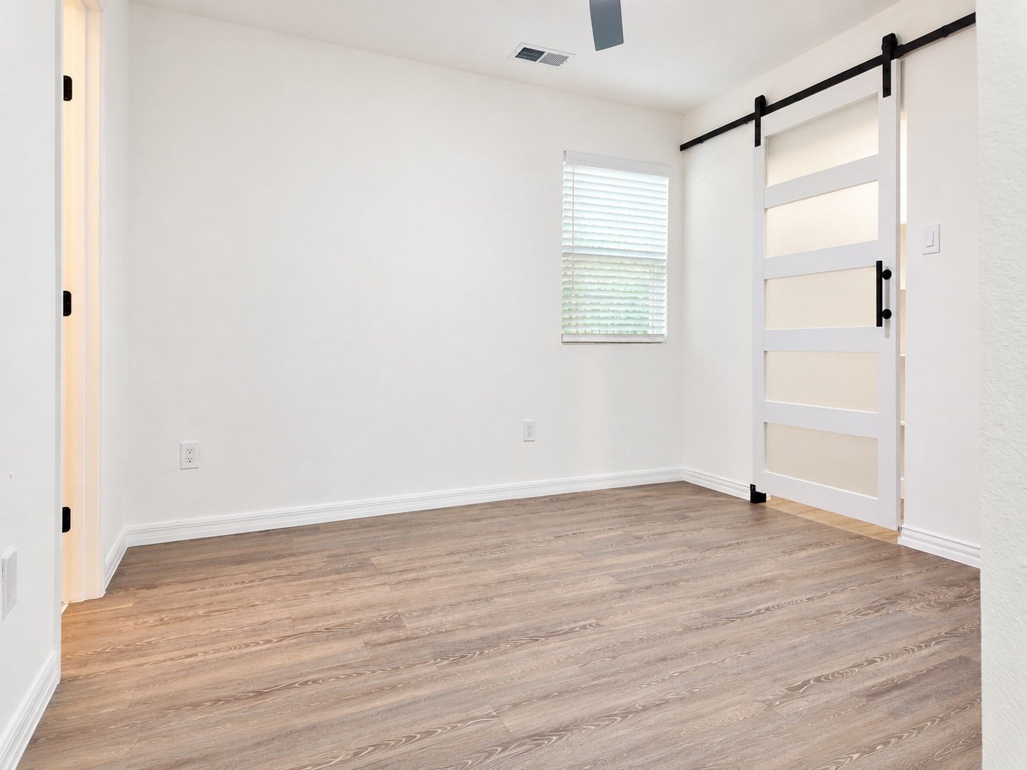 Empty room with wood-look floors, a window with blinds, and a sliding barn door.