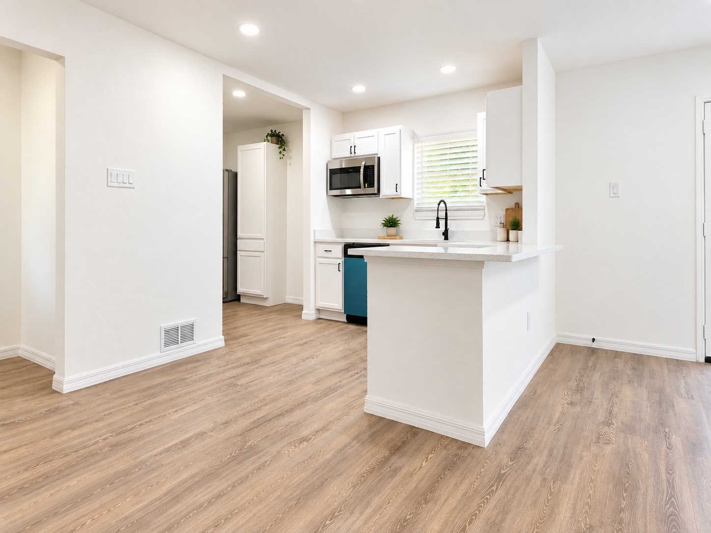 Bright white kitchen with a peninsula counter, stainless steel appliances, and wood-look floors.