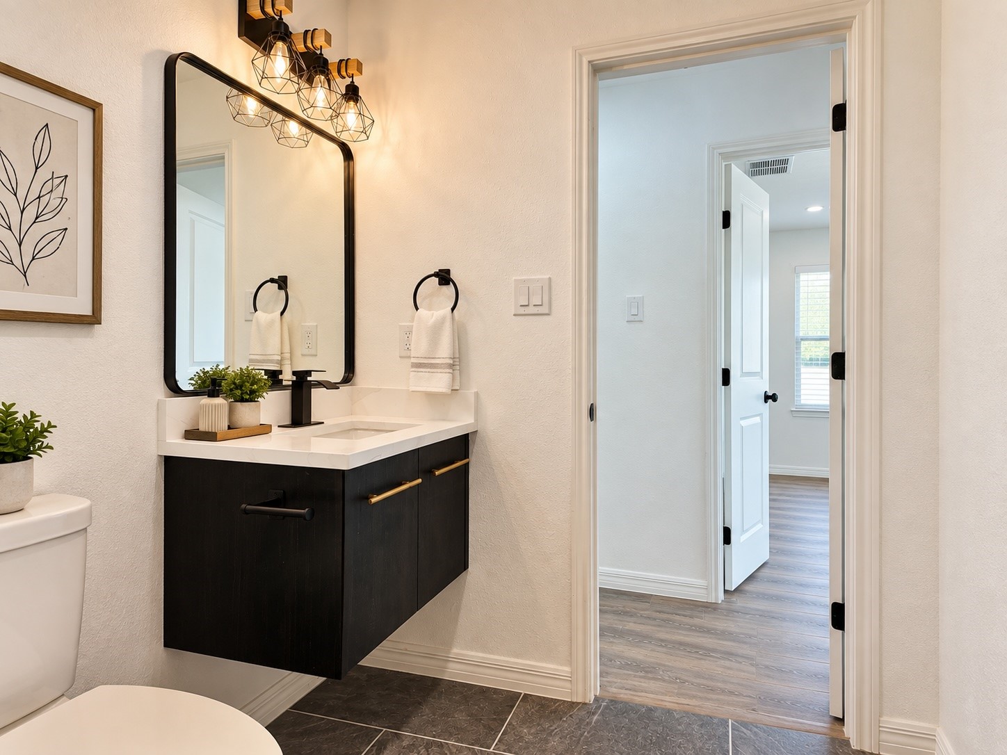Bathroom with a black floating vanity, white countertop, and large mirror beside an open doorway.