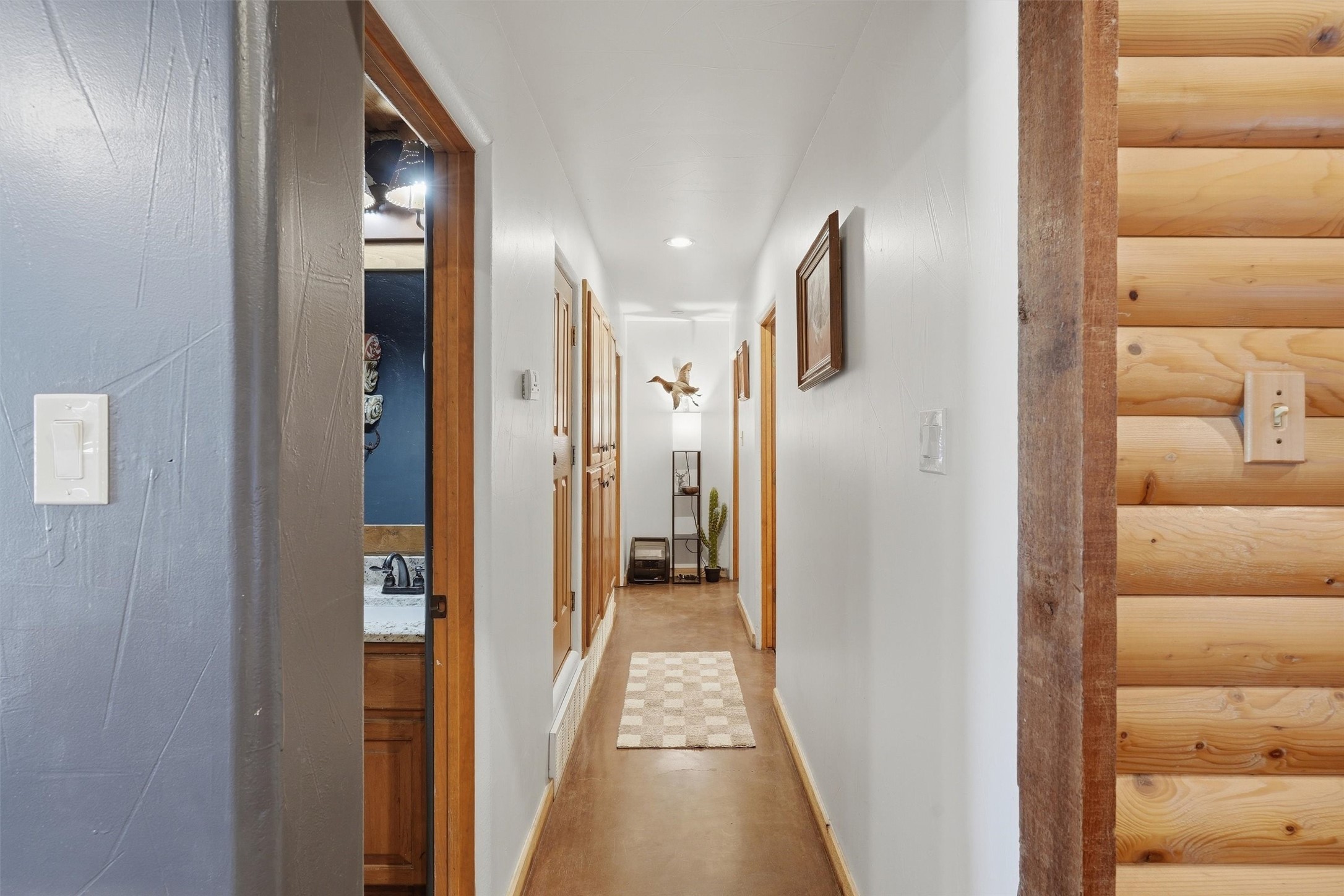 Long white hallway with wood-trimmed doorways, a checkered runner, and a log-style wall.