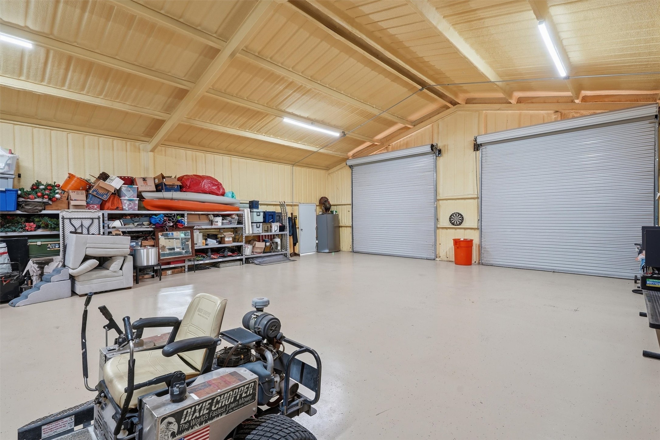 Spacious workshop with two roll-up doors, storage shelves, and a riding lawn mower.