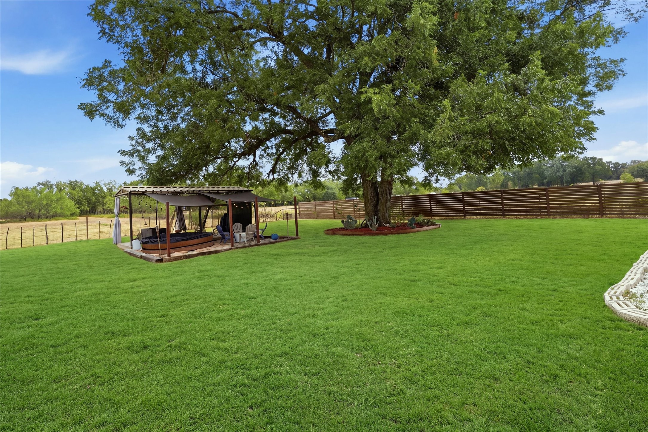 Backyard with a large shade tree, covered seating pavilion, and expansive lawn.