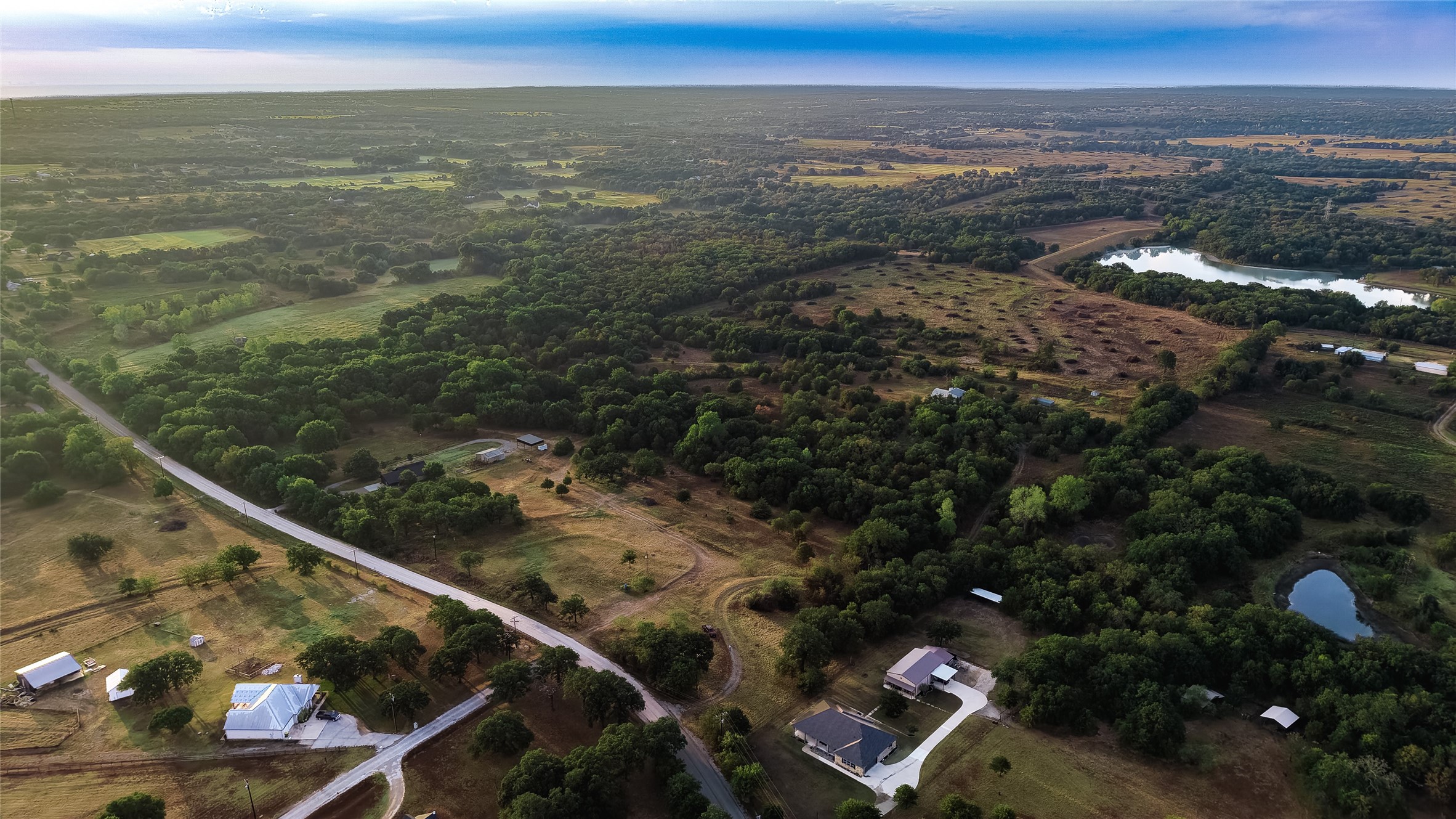 Aerial view of wooded rural acreage with scattered homes, a winding road, and two ponds.