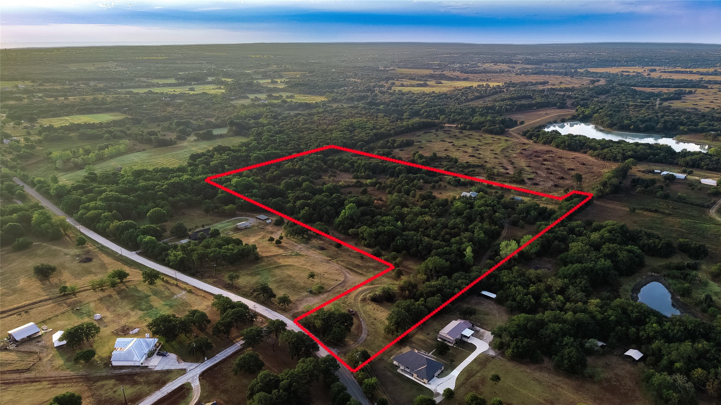 Aerial view of a wooded rural parcel outlined in red, with nearby ponds and roads.