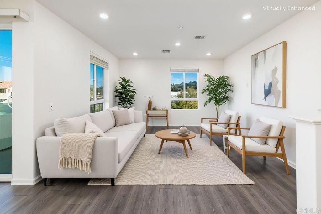 Staged living room with a white sofa, wood-framed armchairs, and large windows.