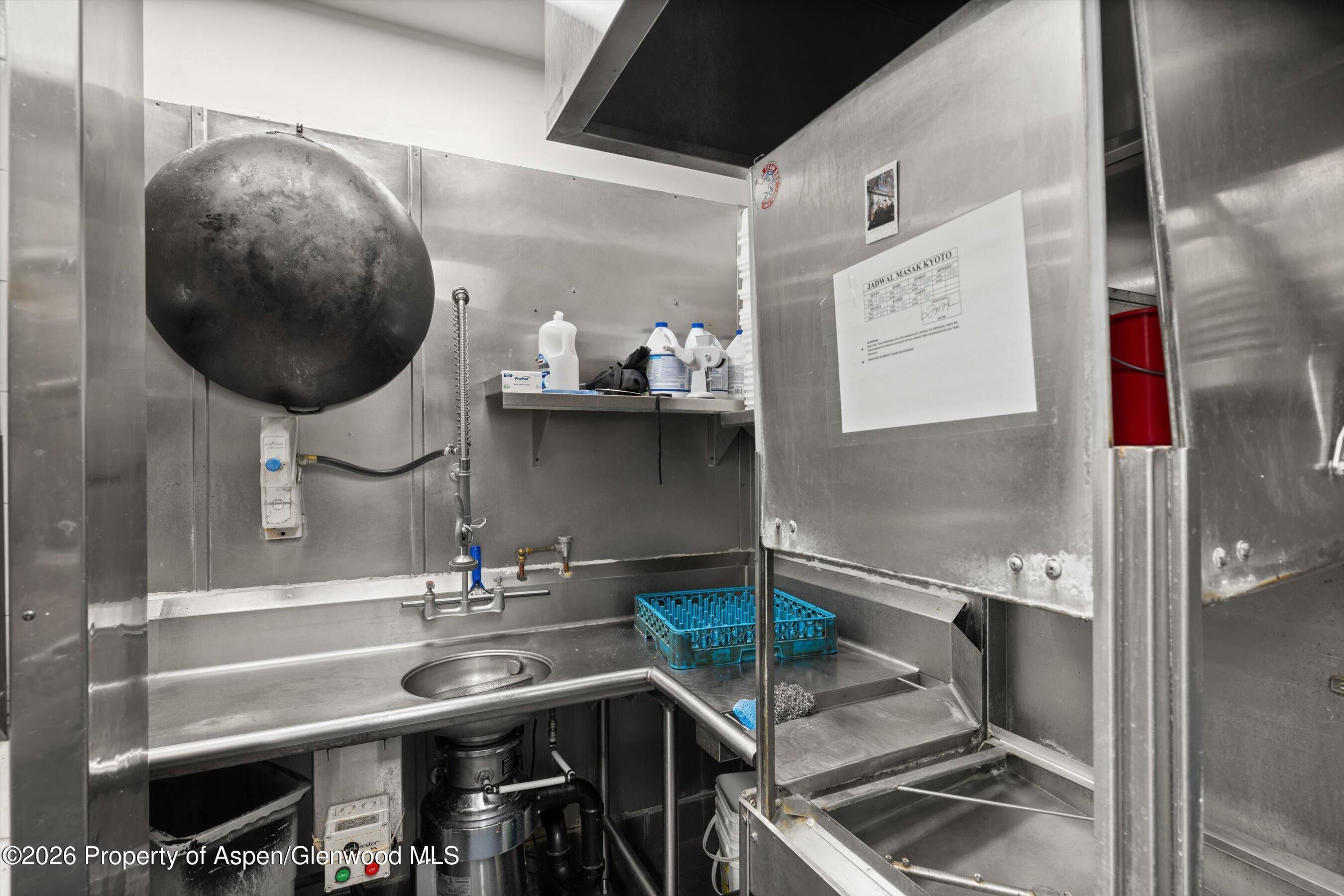 Commercial kitchen dishwashing station with stainless-steel sinks, sprayer, and dish racks.