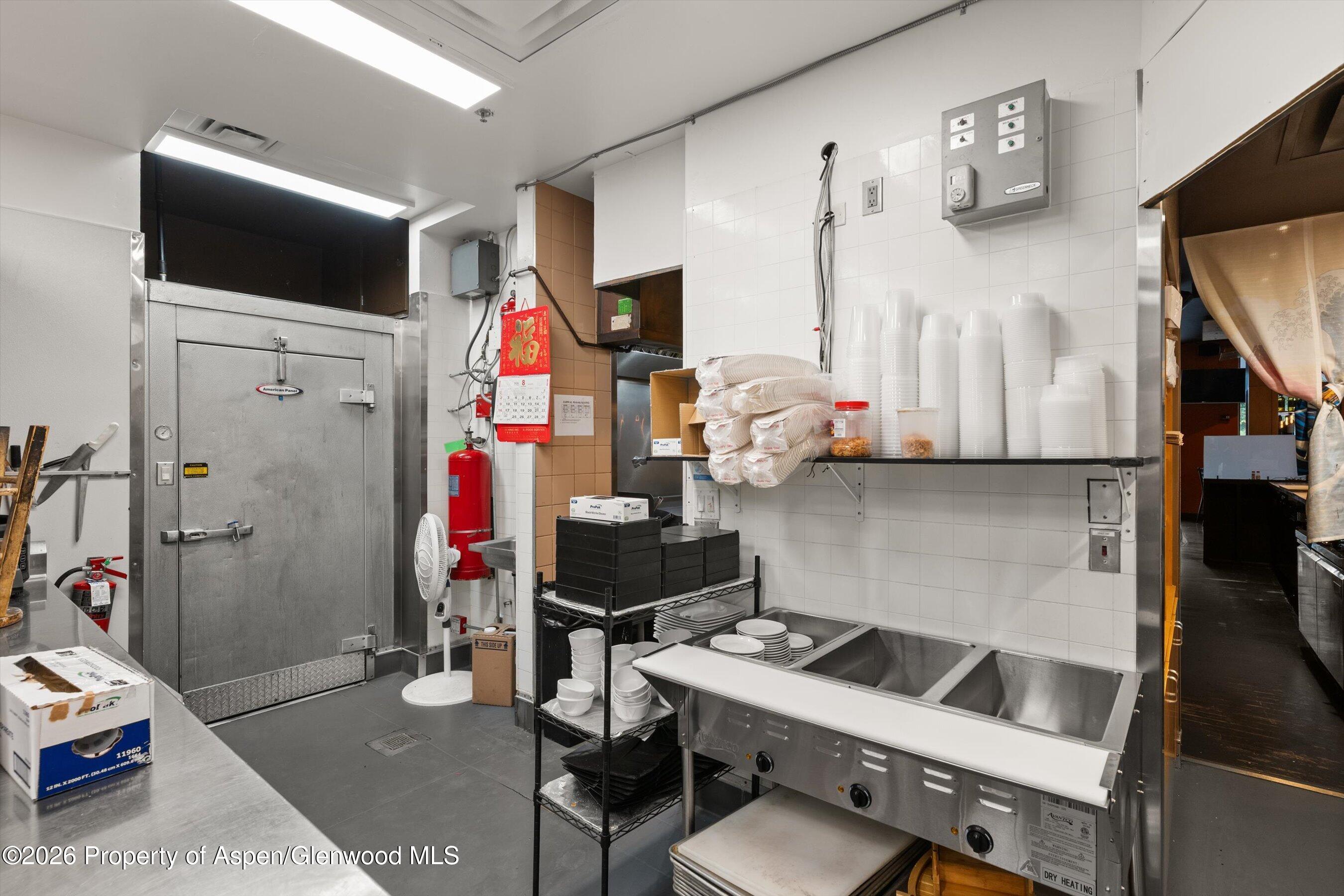 Commercial kitchen with a stainless-steel walk-in cooler, dish racks, and a large multi-compartment sink.
