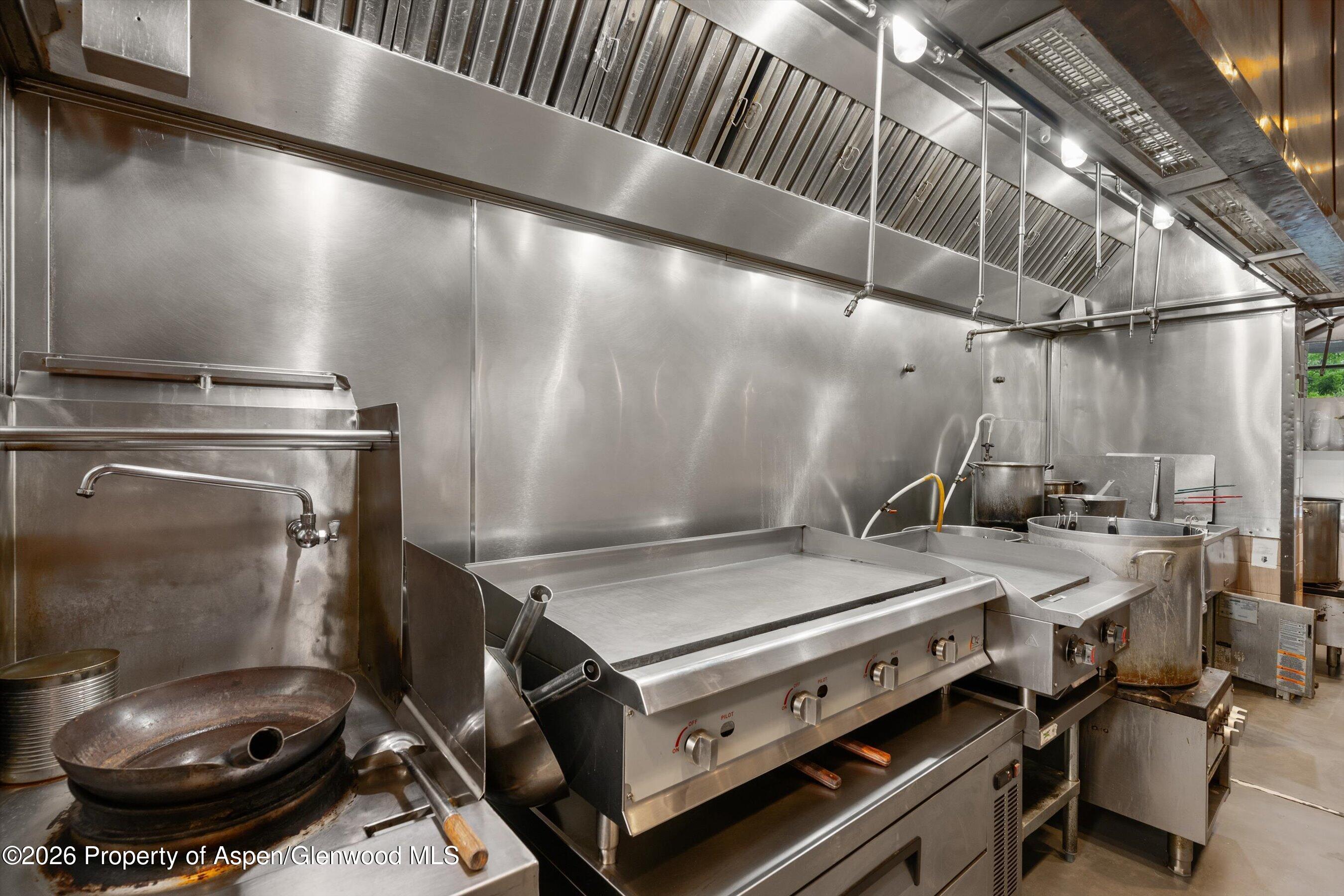 Commercial kitchen with stainless steel appliances, a large flat-top griddle, and an overhead ventilation hood.