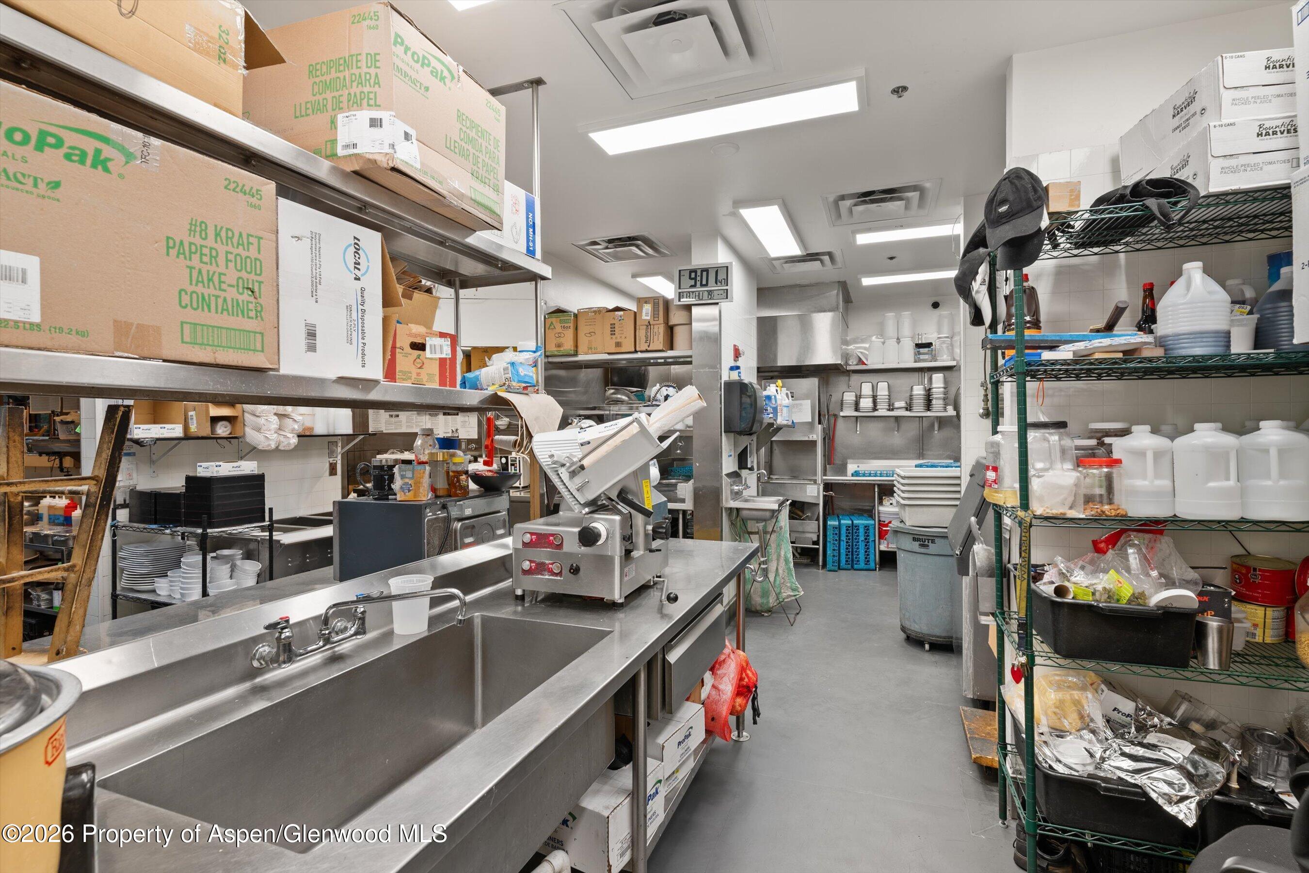 Commercial kitchen with stainless-steel worktables, food-processing equipment, and densely stocked shelves.