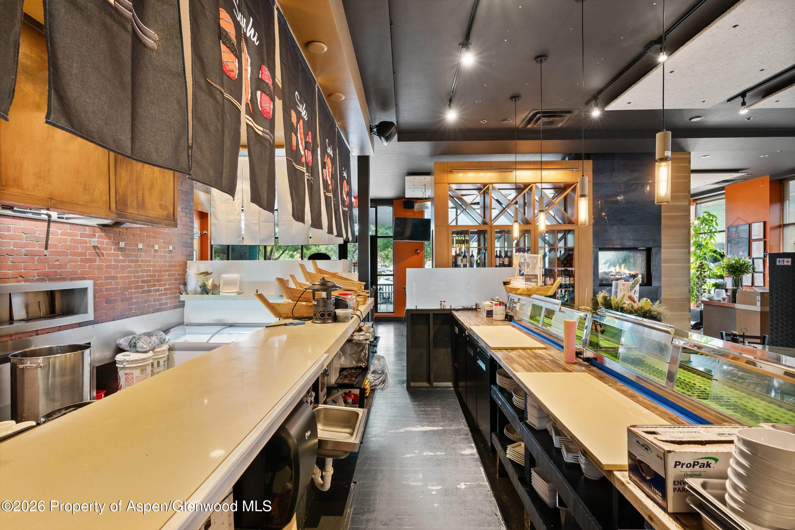 Commercial restaurant kitchen with long service counters, glass food displays, and a wood-framed wine cabinet.
