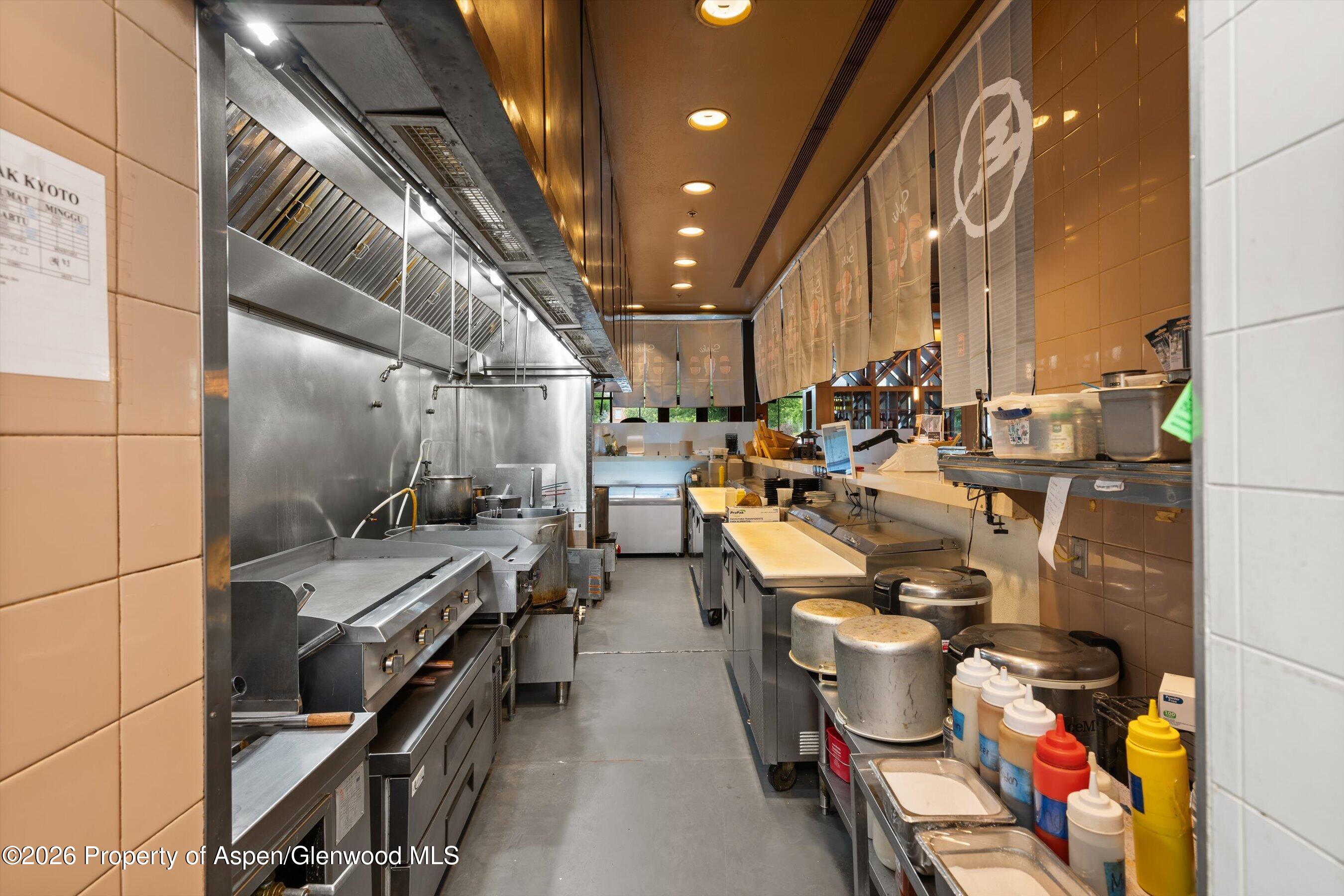 Commercial kitchen with stainless-steel cooking line, overhead ventilation hood, and condiment bottles along the service counter.
