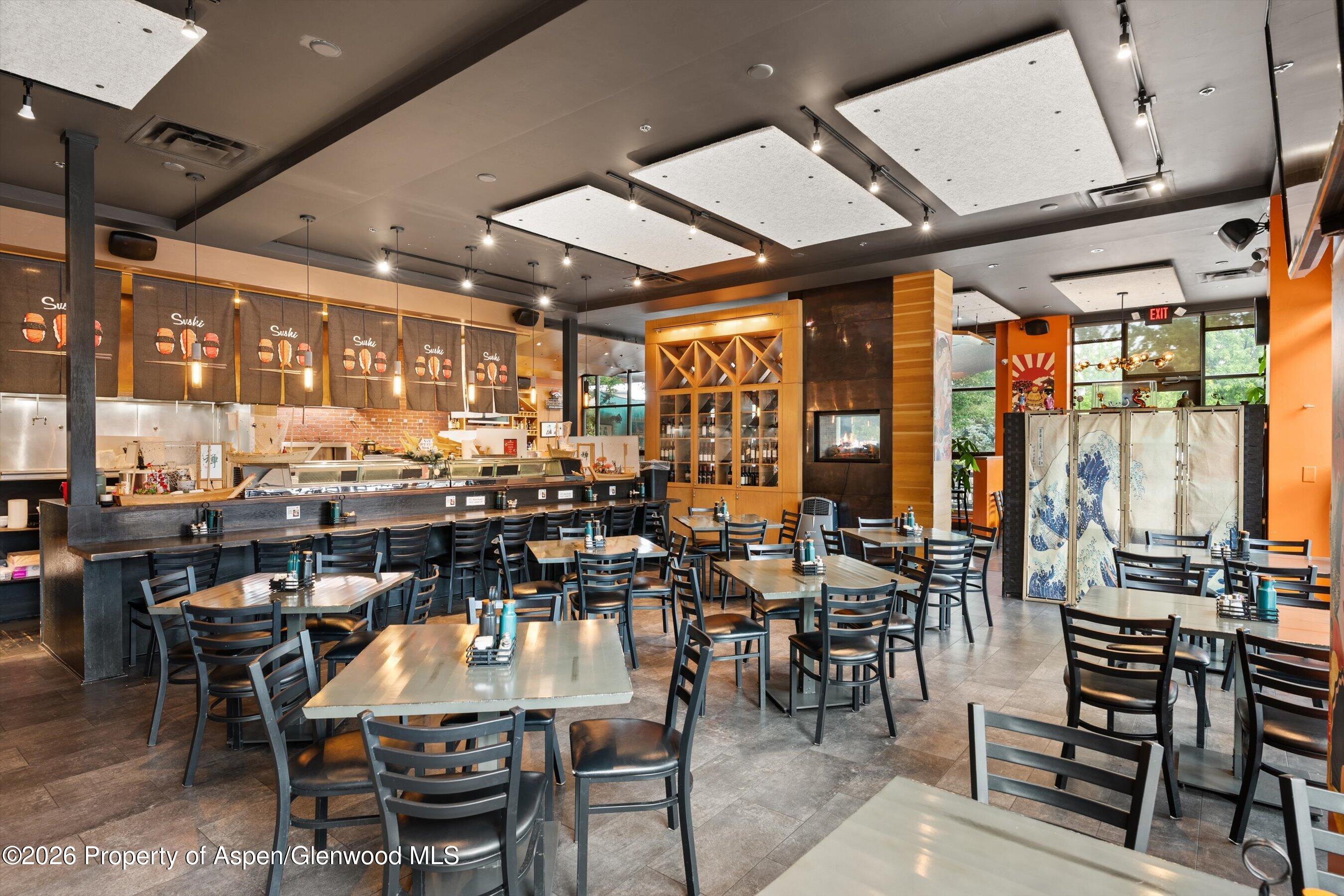 Sushi restaurant dining room with a long counter, wooden wine display, and decorative folding screen.