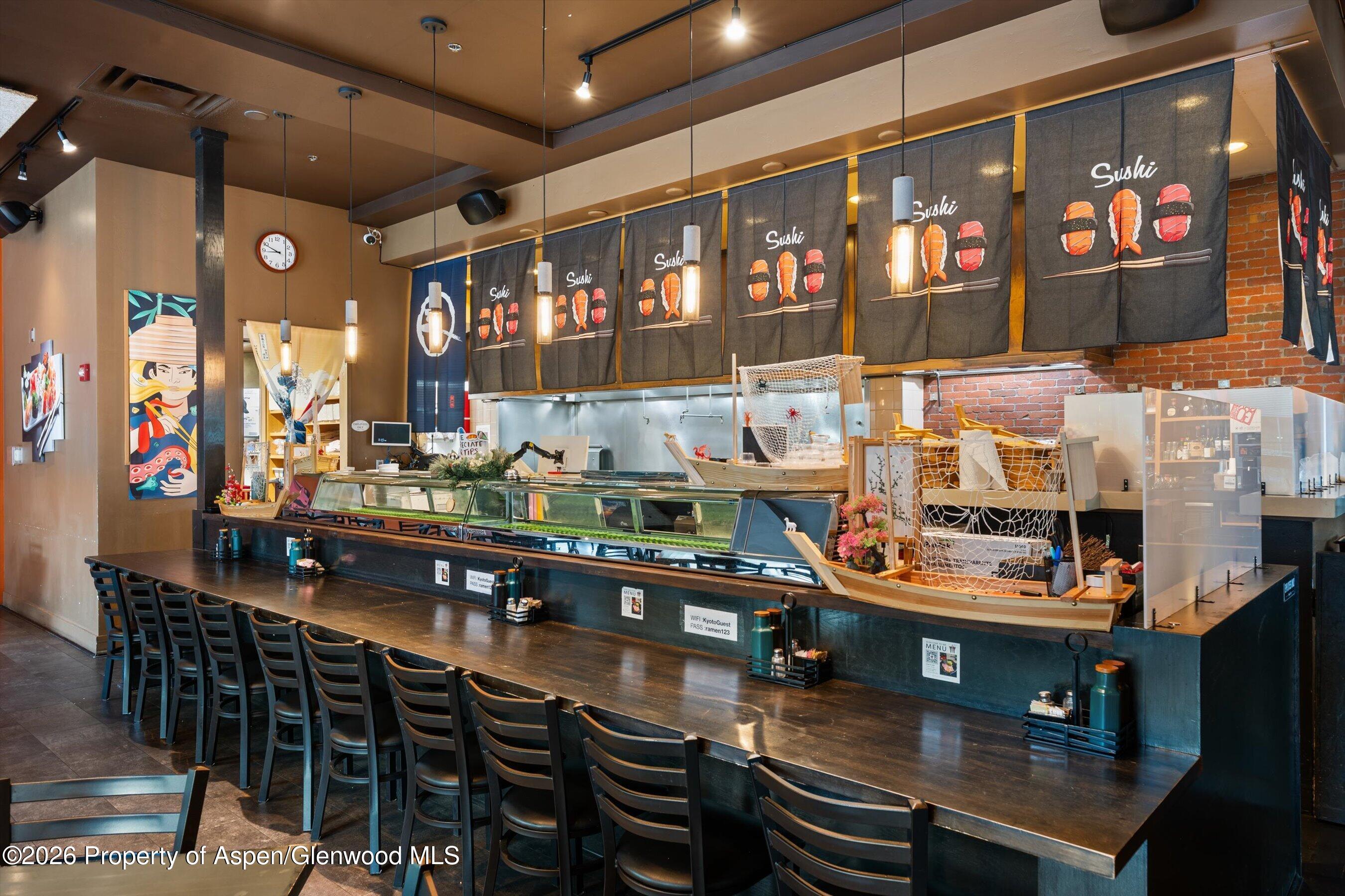 Sushi restaurant interior with a long counter, glass display case, pendant lights, and illustrated fabric screens.