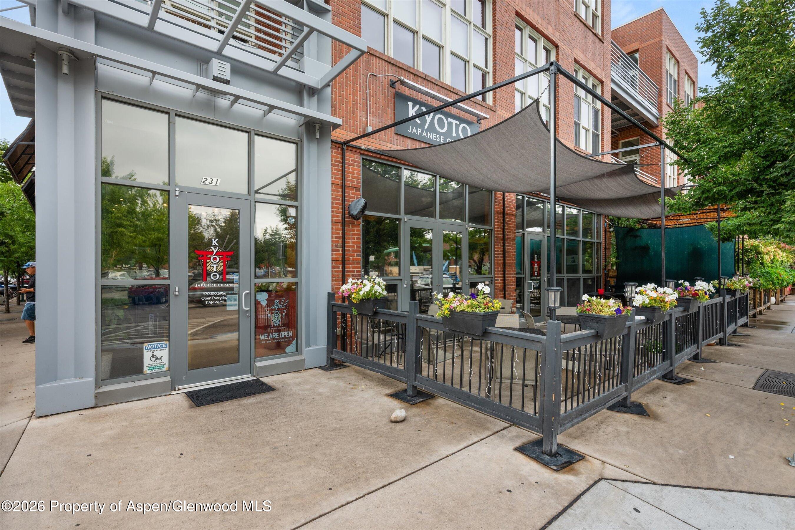 Commercial storefront with a flower-lined patio, dark railings, and large shade canopies.
