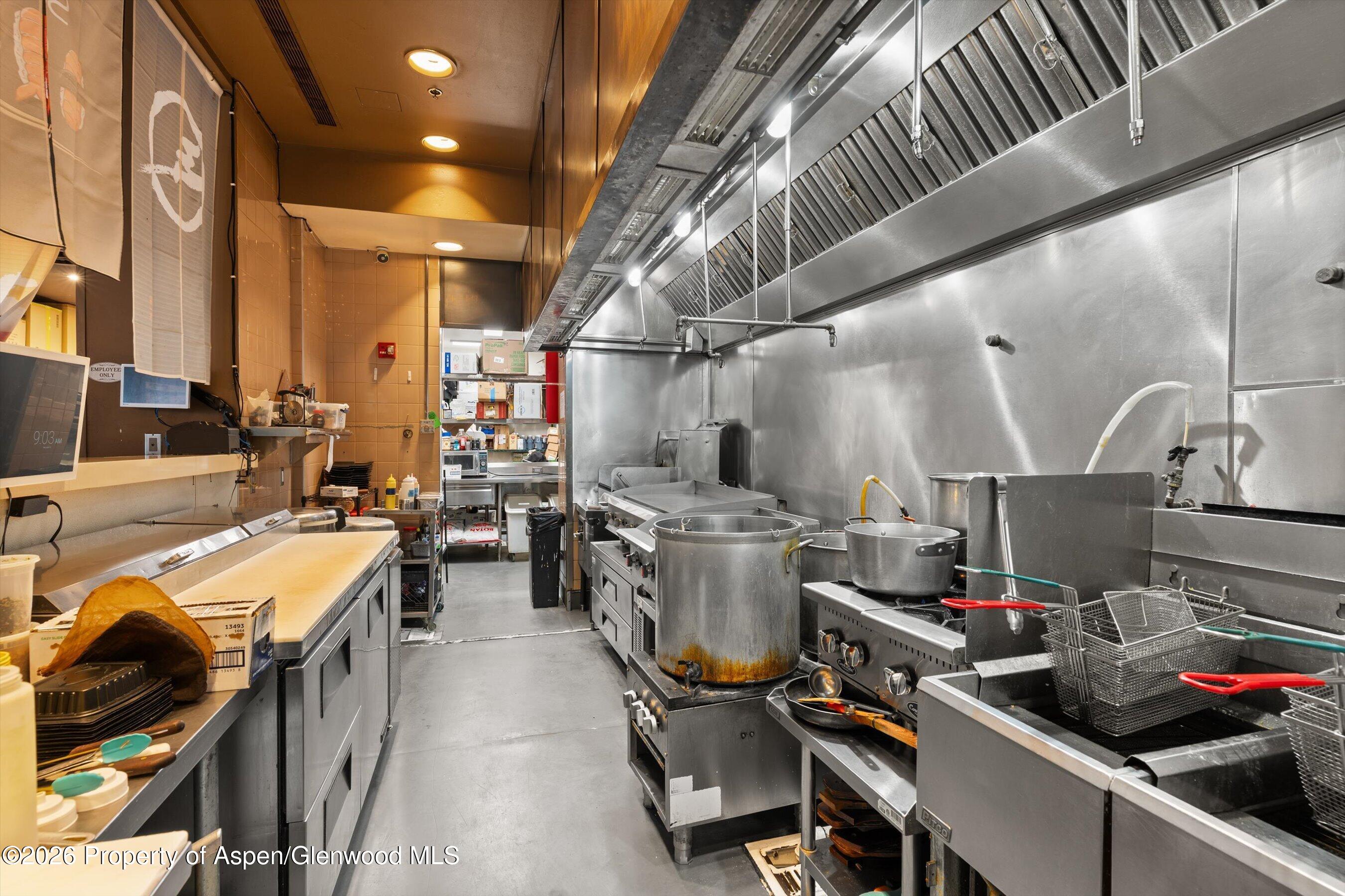 Commercial kitchen with stainless-steel cooking line, large exhaust hood, fryers, and prep counters.