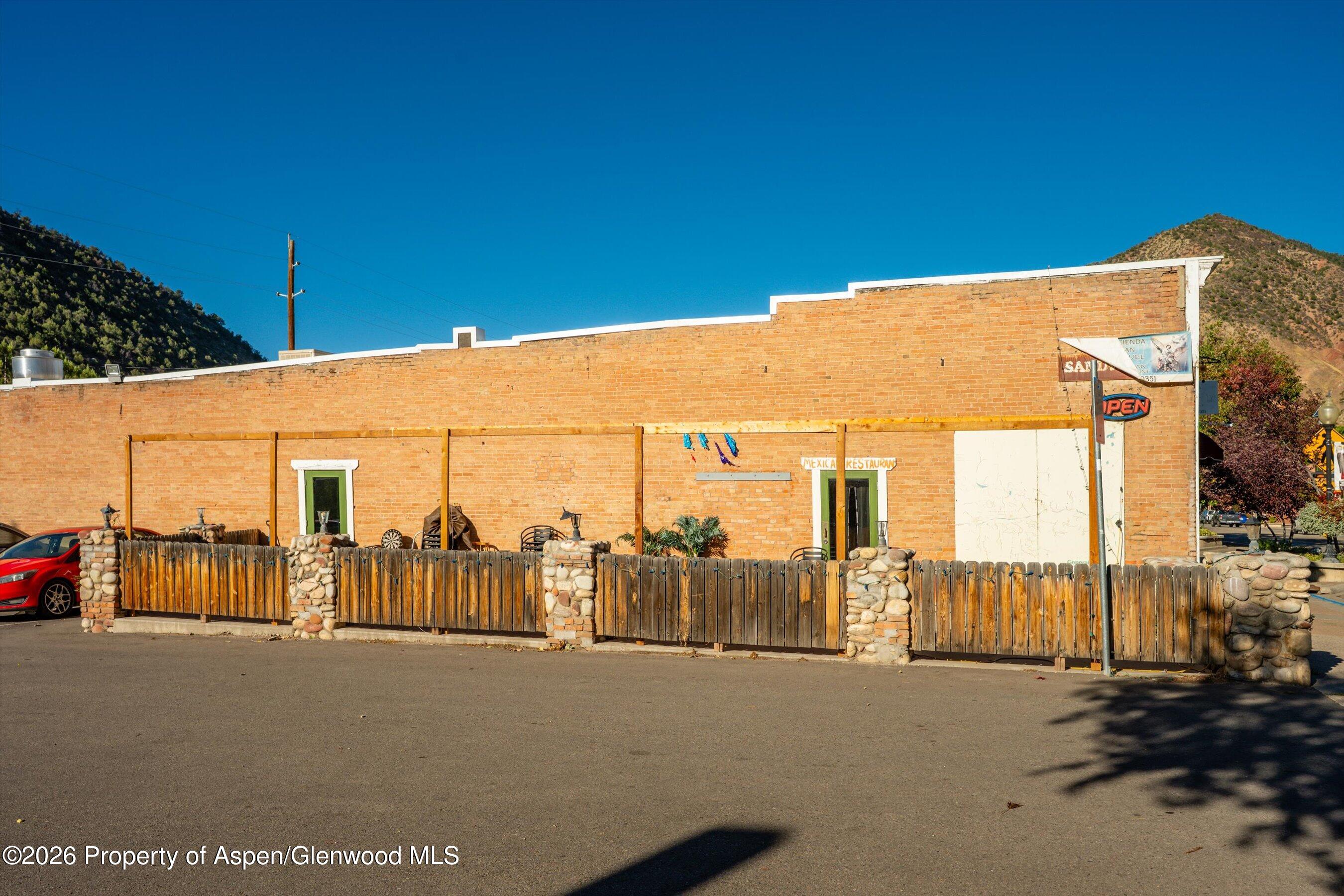 Brick restaurant storefront with a fenced outdoor patio and mountains behind it.