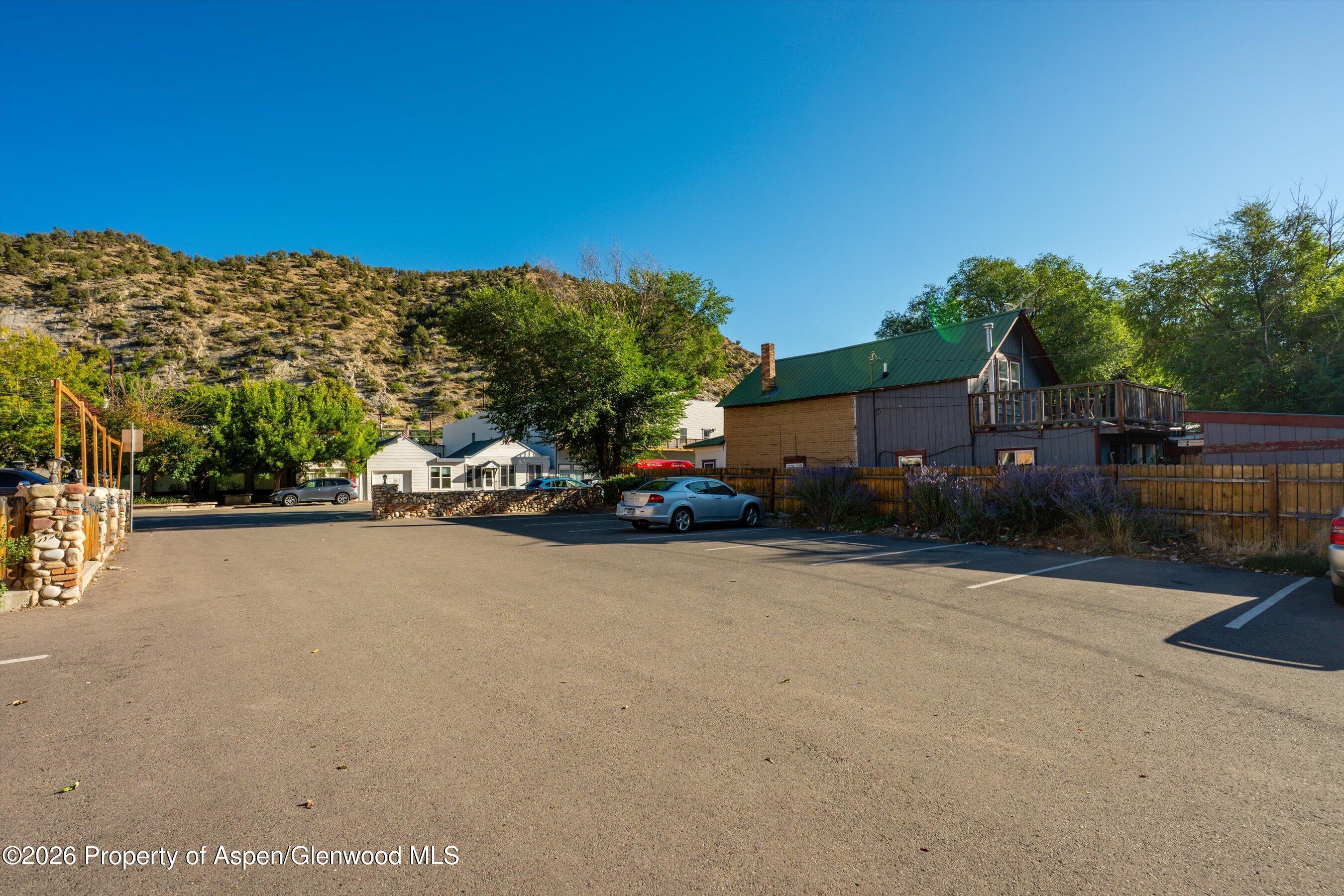 Commercial building with a raised deck beside a spacious paved parking lot and rocky hillside.