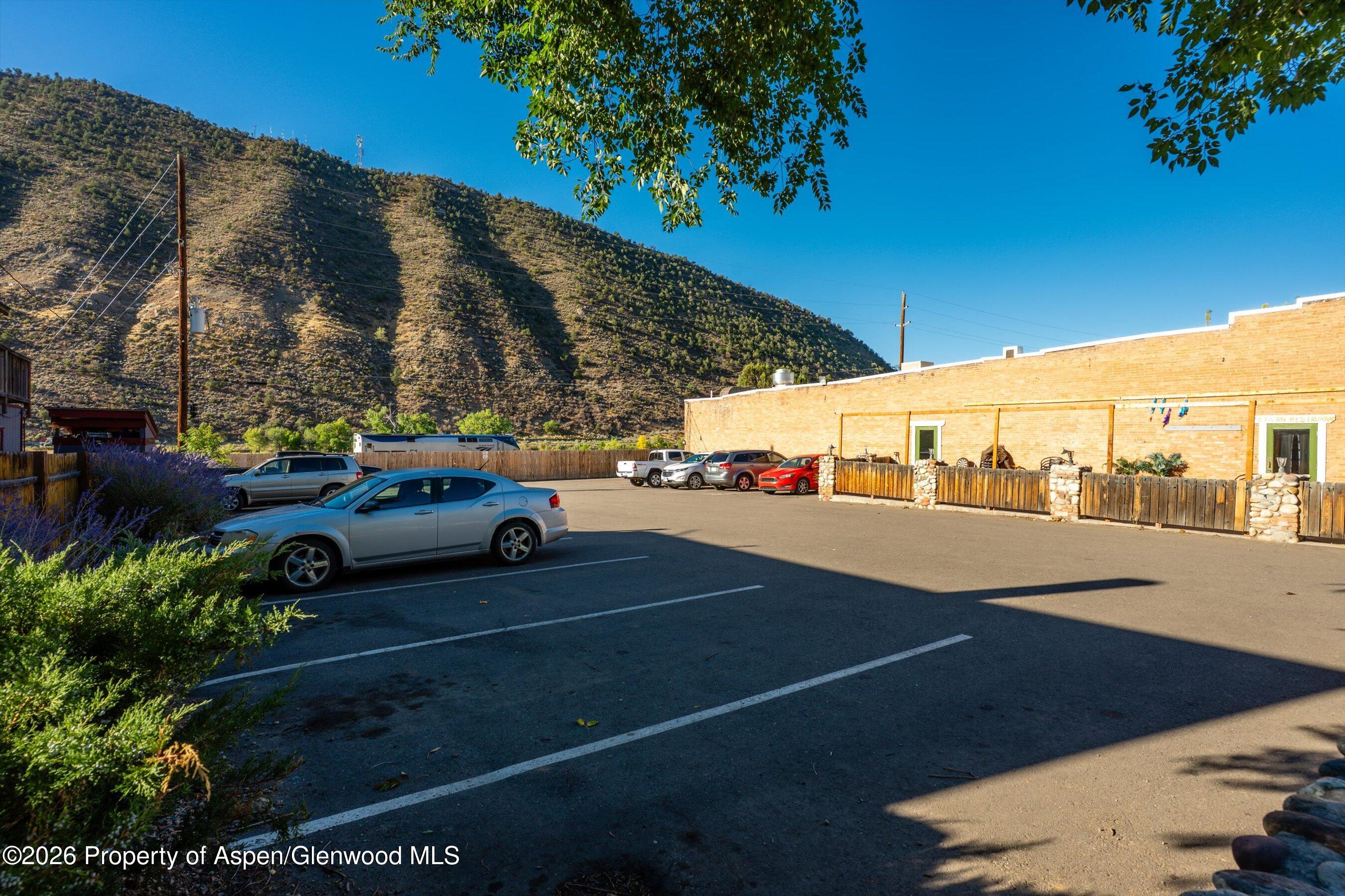 Commercial building and parking lot at the base of a shrub-covered hillside.