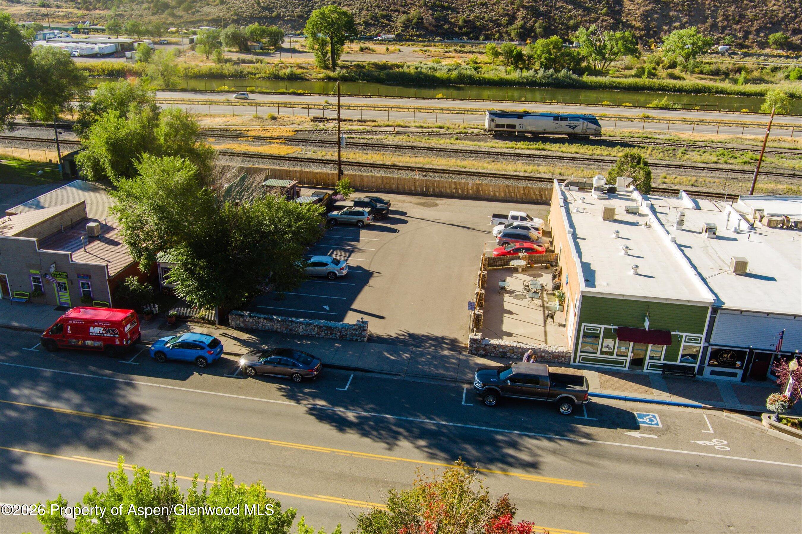 Aerial view of a downtown commercial lot with parking, storefronts, railroad tracks, and a river.