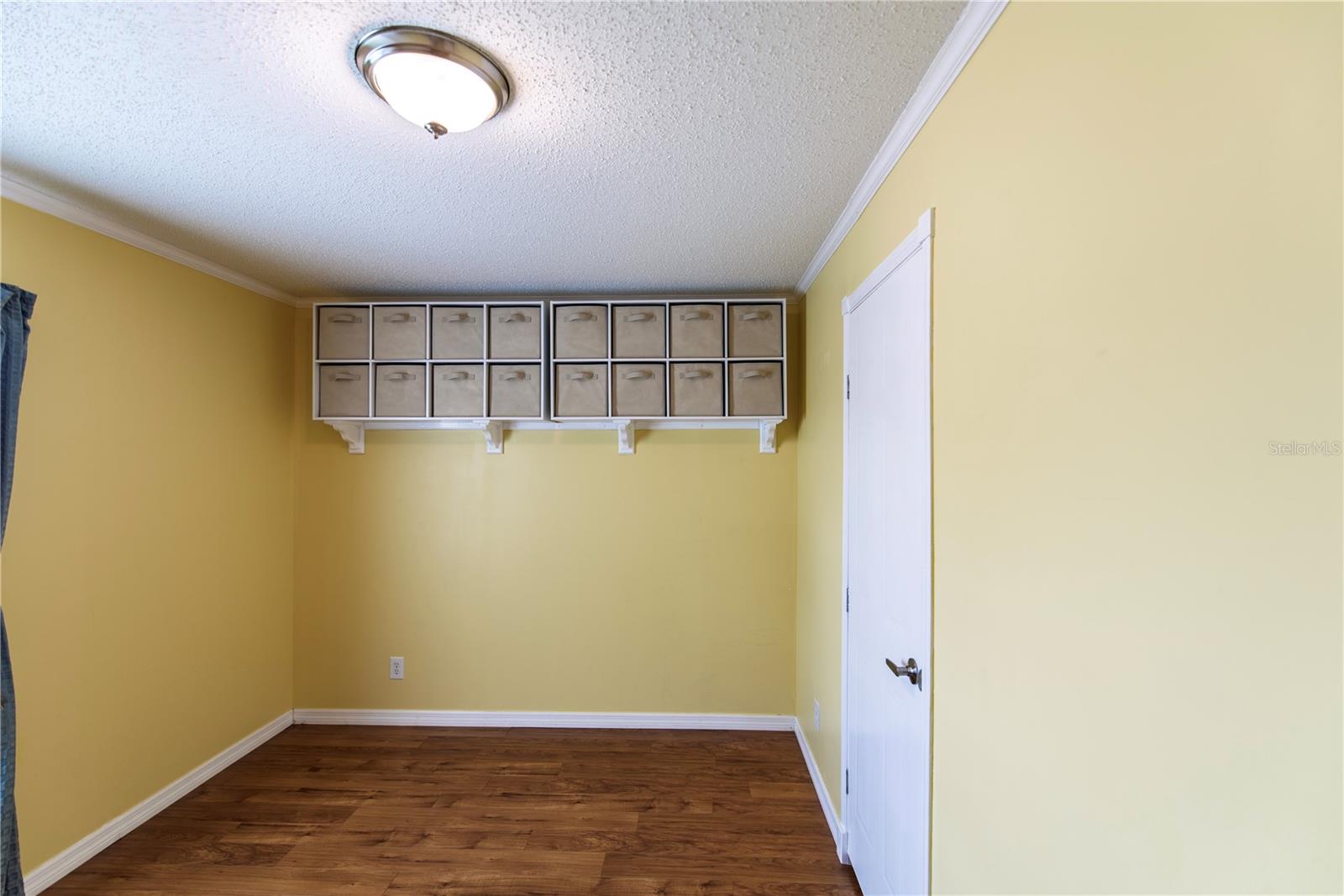 Narrow yellow room with hardwood floors and wall-mounted shelves of fabric storage bins.