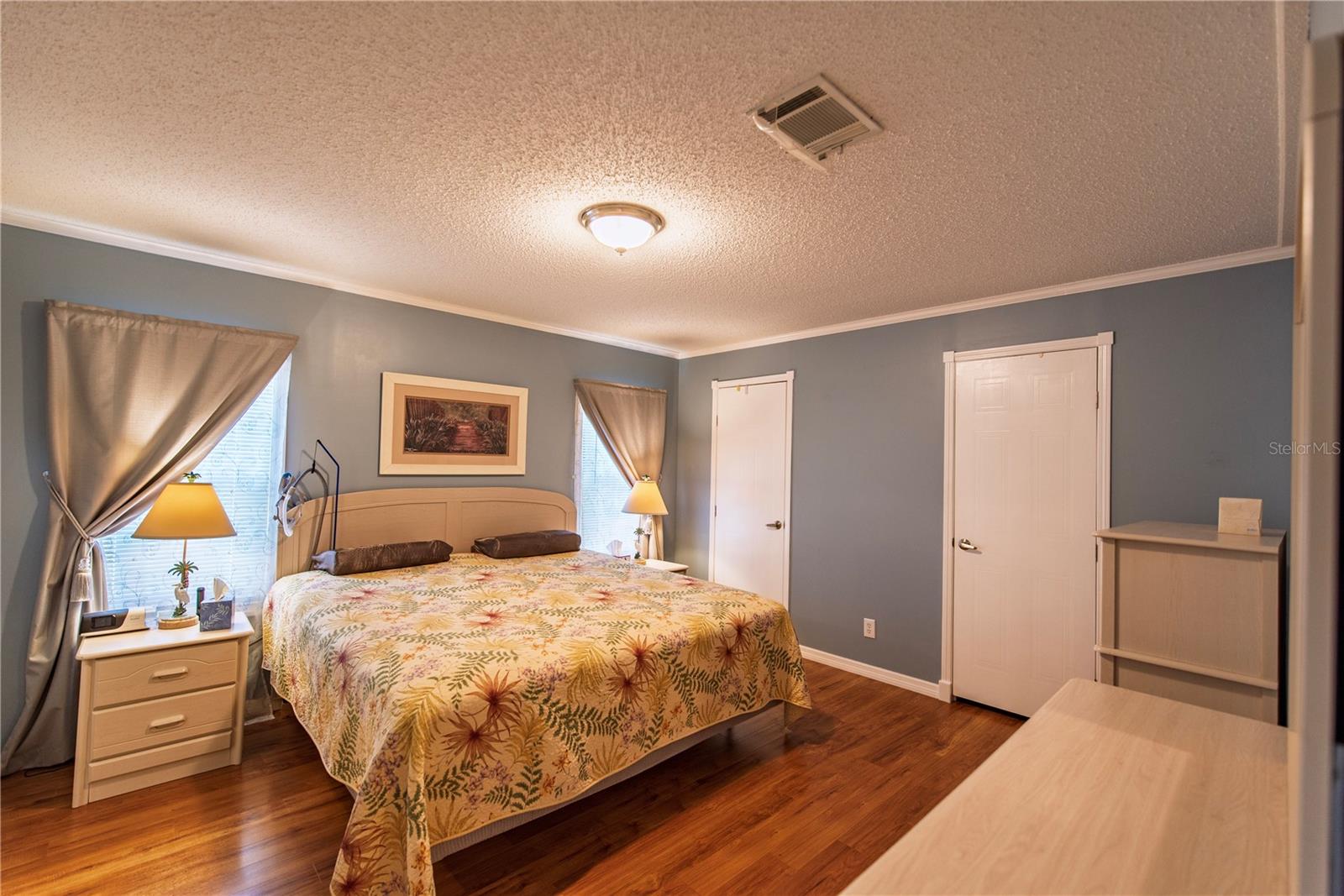 Bedroom with a floral-covered bed, blue-gray walls, and warm hardwood floors.
