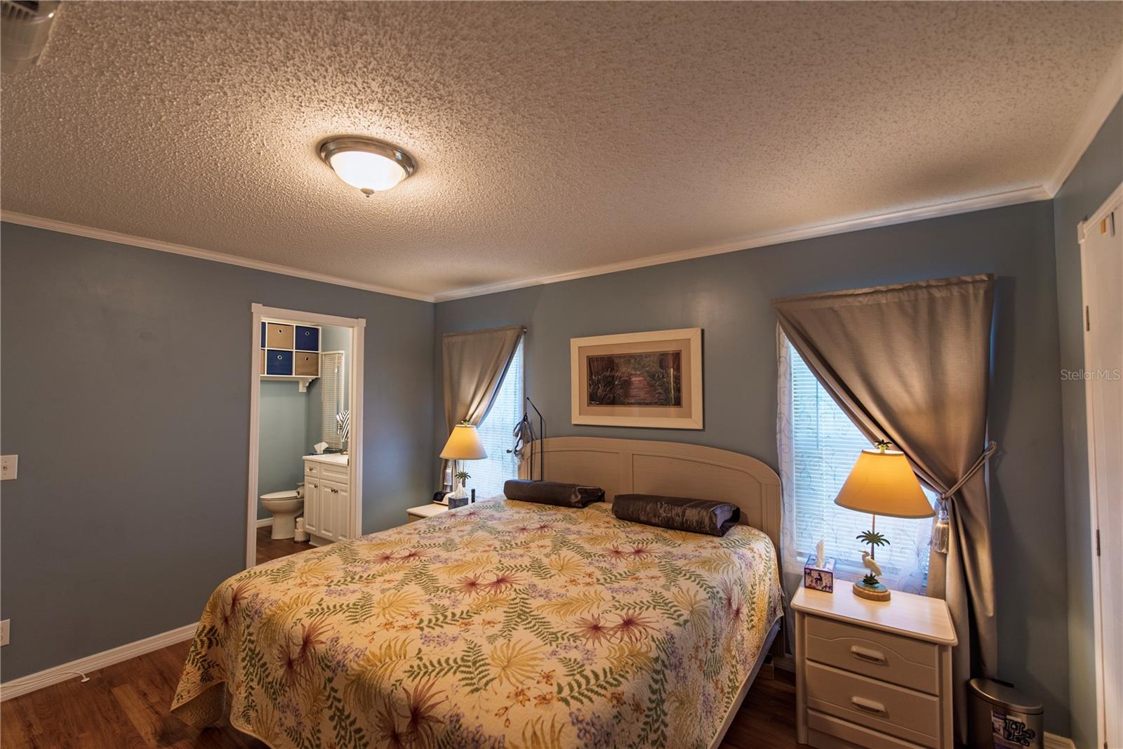 Furnished bedroom with a floral bedspread and an adjoining bathroom visible through the doorway.