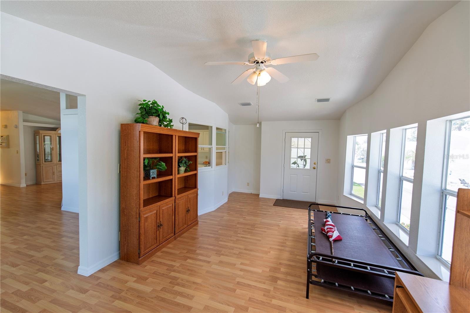 Bright room with tall windows, wood flooring, a ceiling fan, wooden cabinet and daybed.