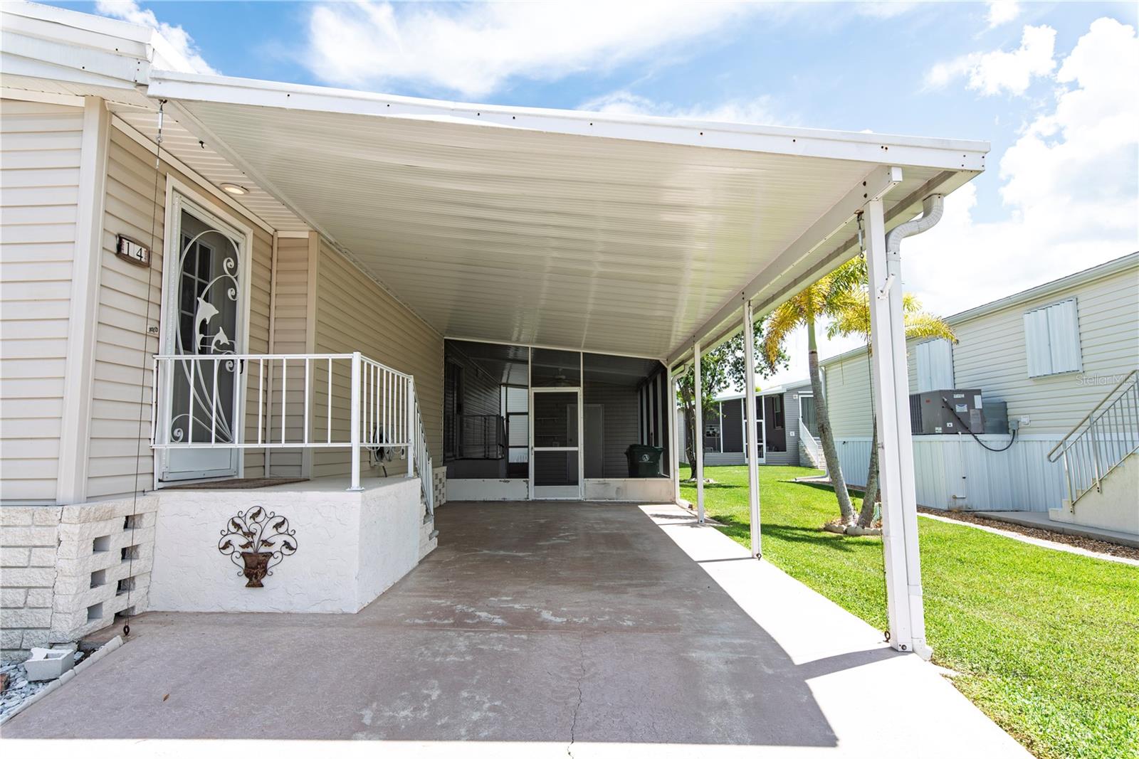 Manufactured home with a long covered carport, concrete parking pad, and decorative security screen door.