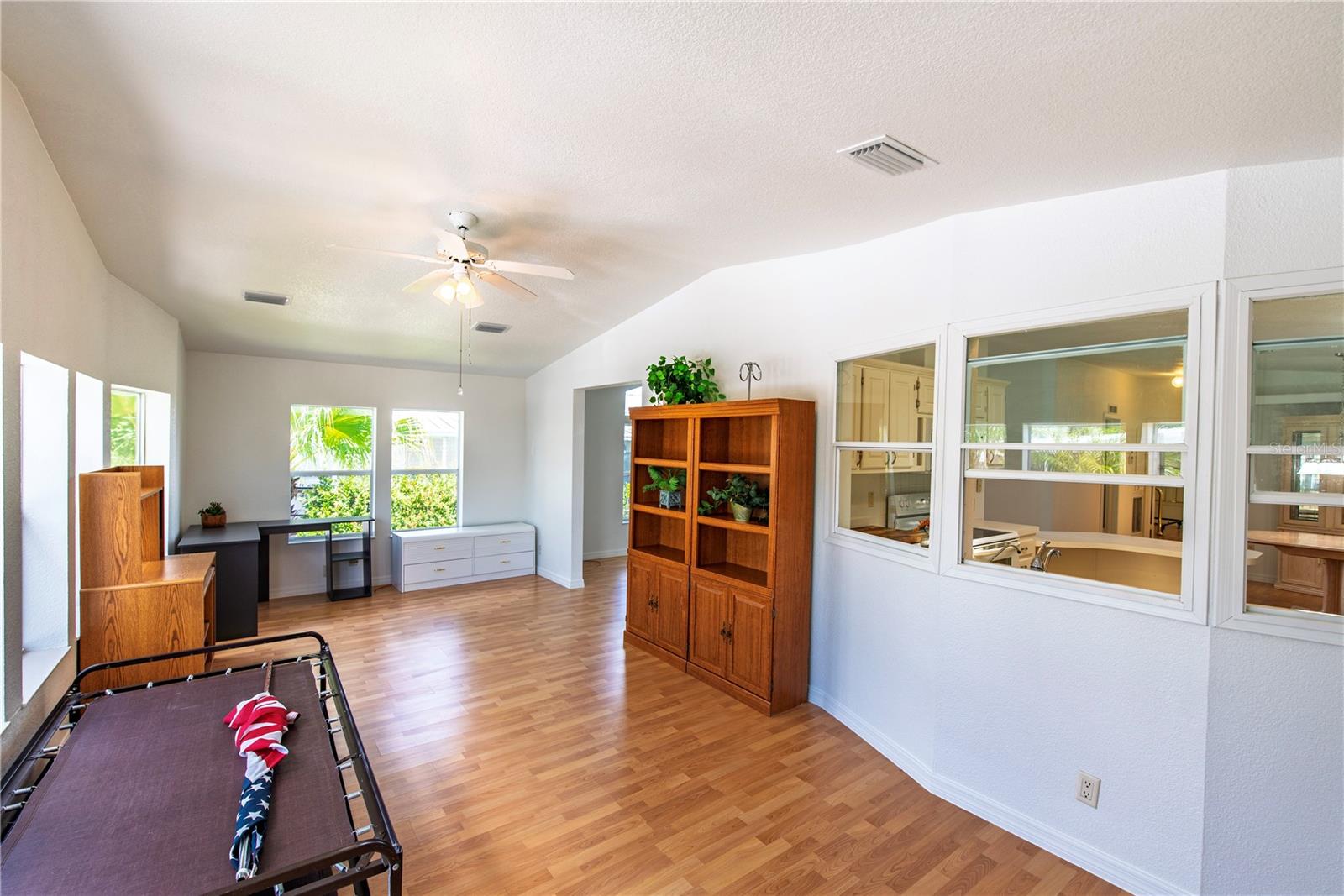 Bright bonus room with wood flooring, a ceiling fan, and windows opening to the kitchen.