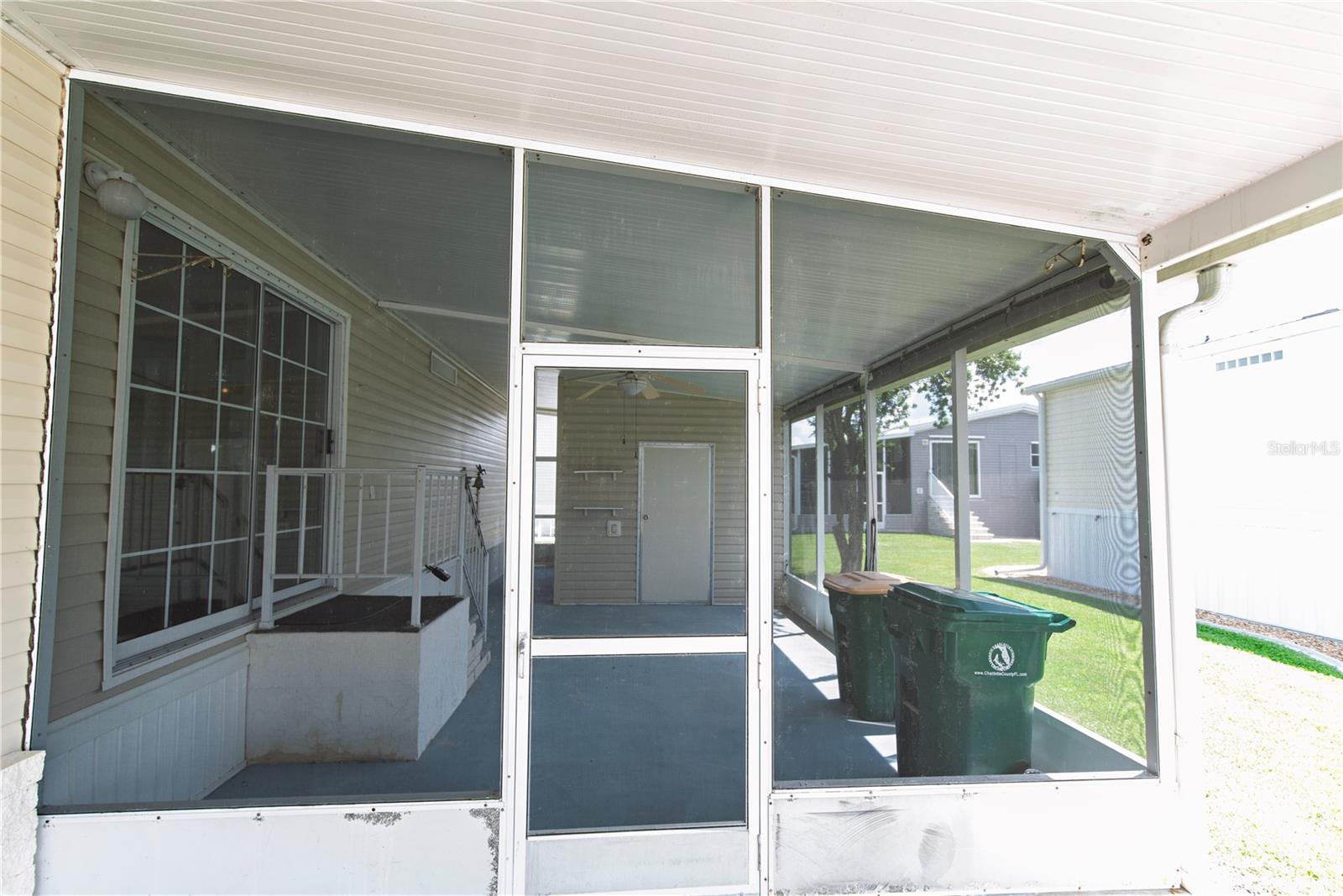 Screened porch with a central screen door and green wheeled bins.