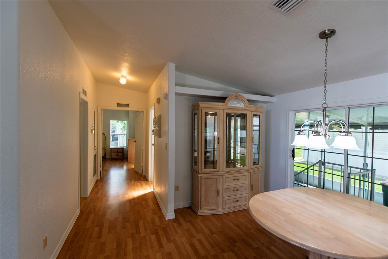 Dining area with a round wood table and glass-front china cabinet beside a hallway.