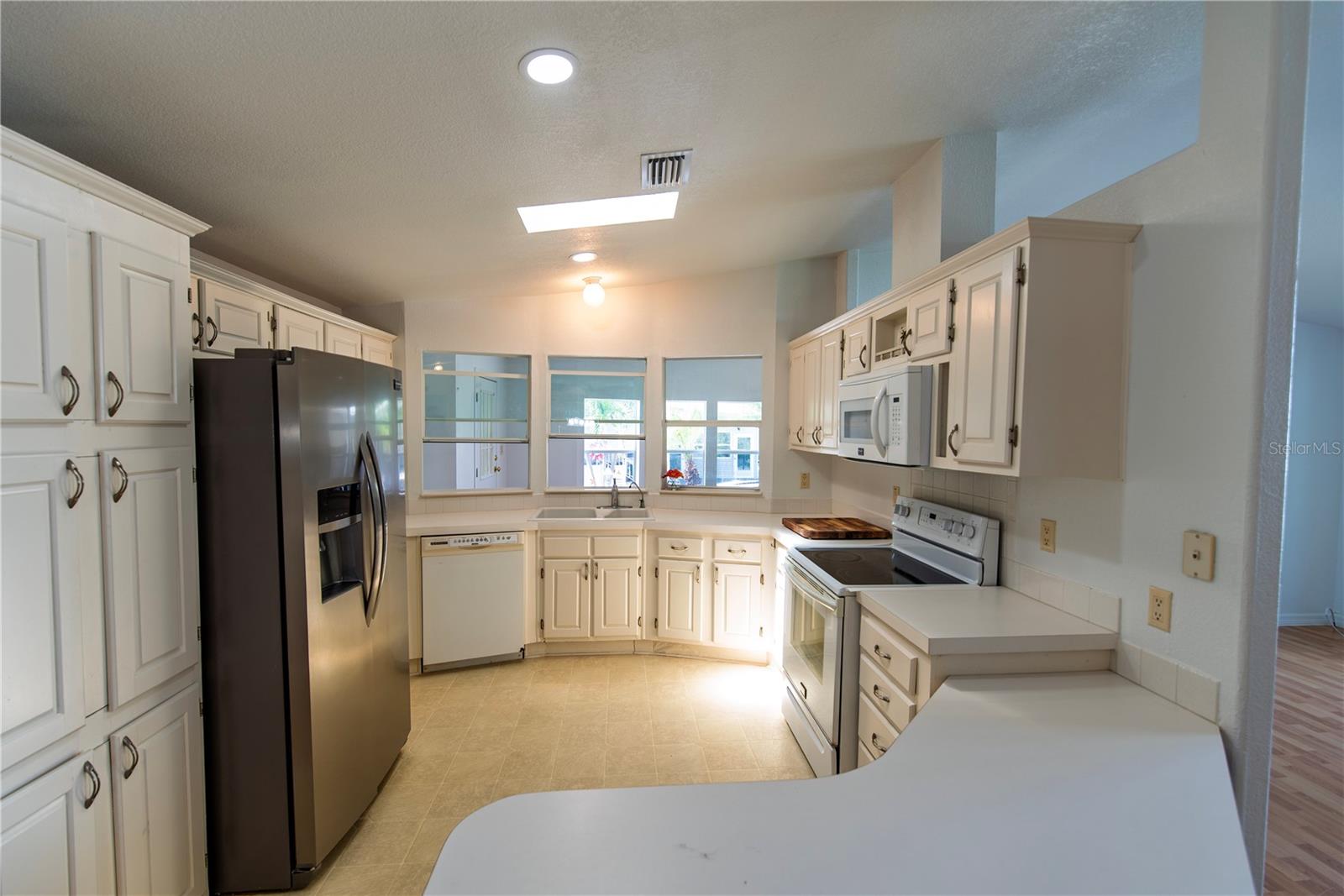 Kitchen with white cabinets, stainless steel appliances, and a sink beneath three windows.