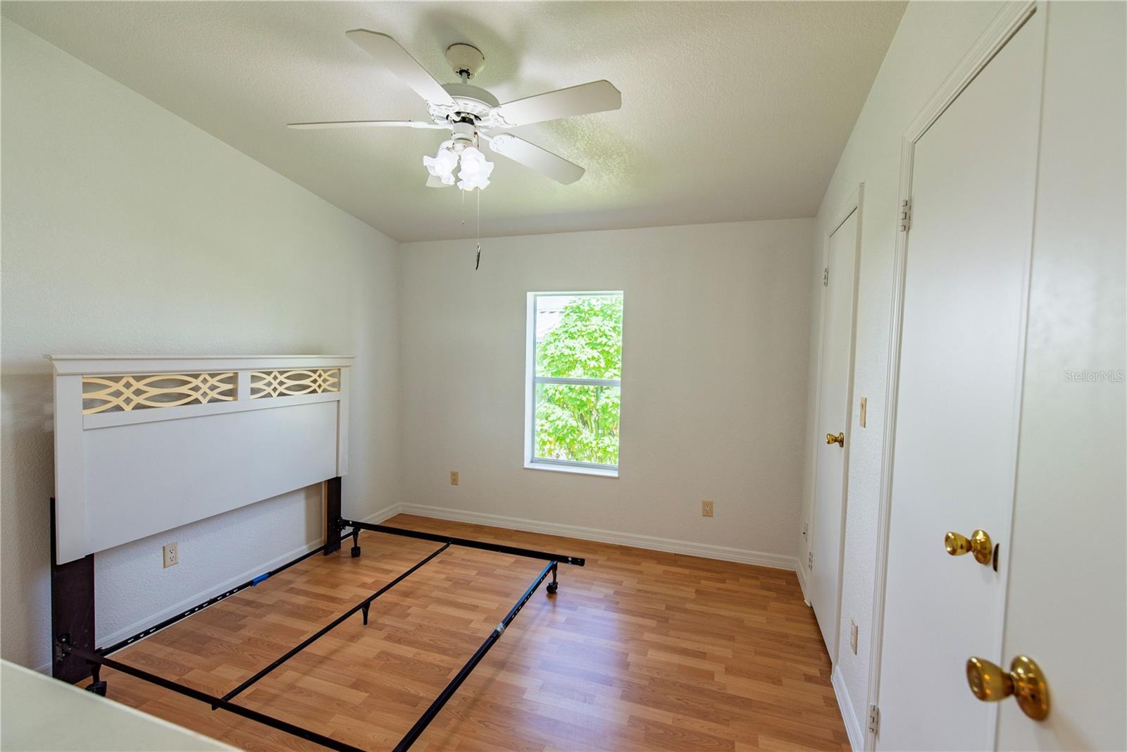 Bedroom with wood-look flooring, a ceiling fan, and a decorative headboard on an exposed bed frame.