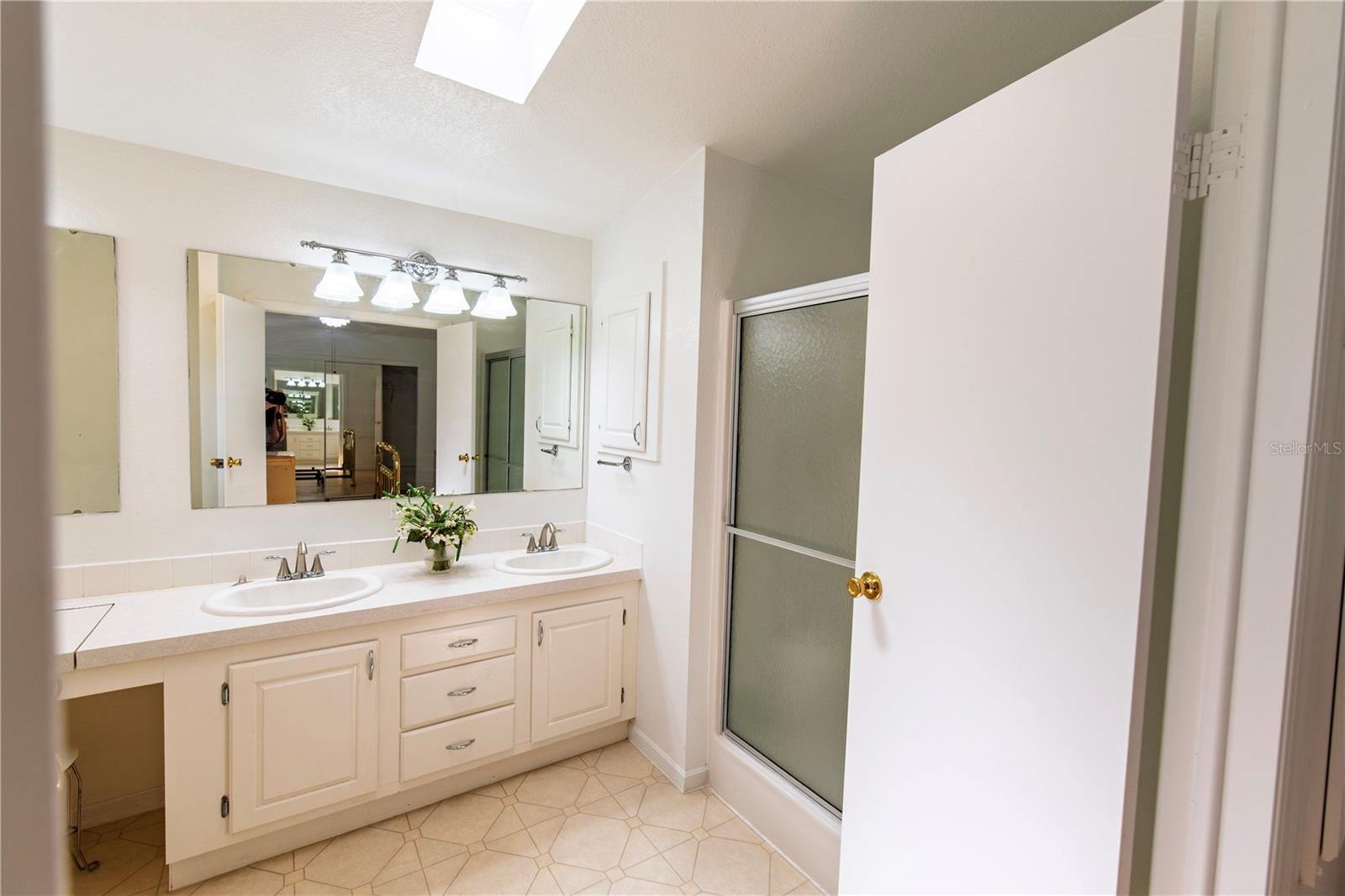 Bathroom with a white double-sink vanity, large mirror, and frosted-glass shower enclosure.