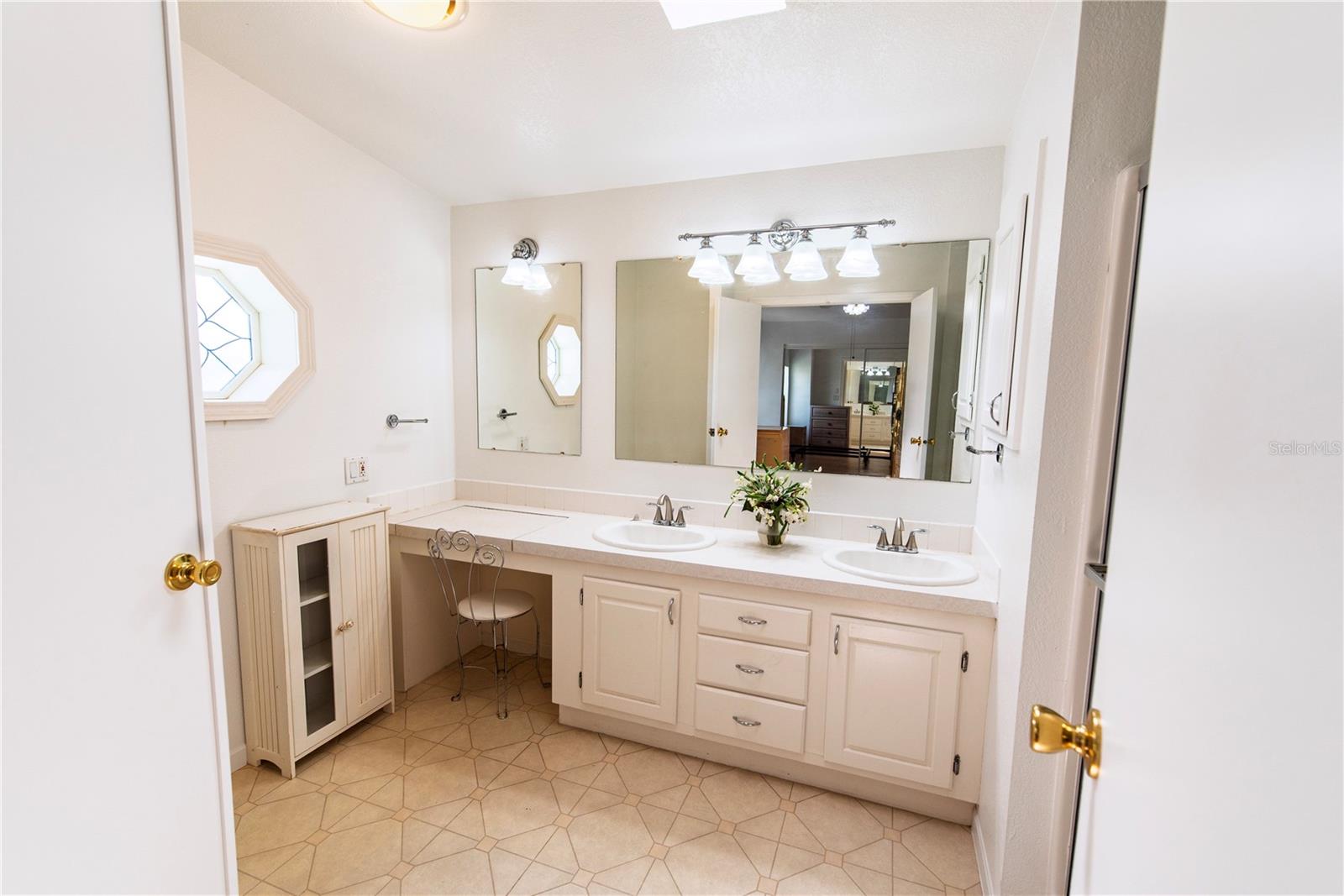 Bathroom with a white double-sink vanity, large mirror, and octagonal window.
