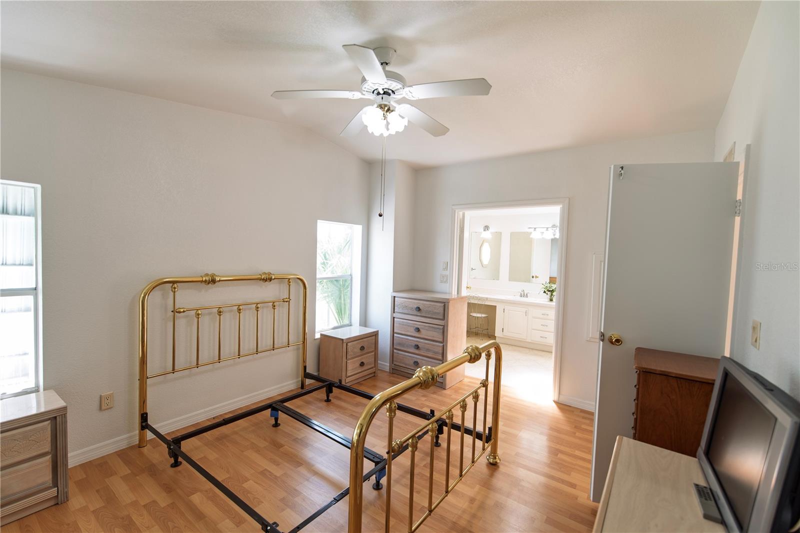 Bedroom with a brass bed frame, wood-look flooring, and an open doorway to a bright bathroom.