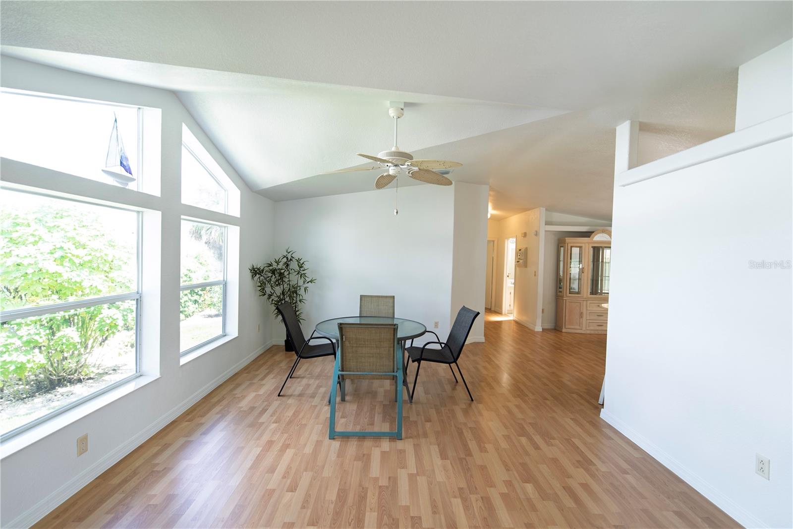 Dining area with a glass-top table beneath a vaulted ceiling and tall windows.