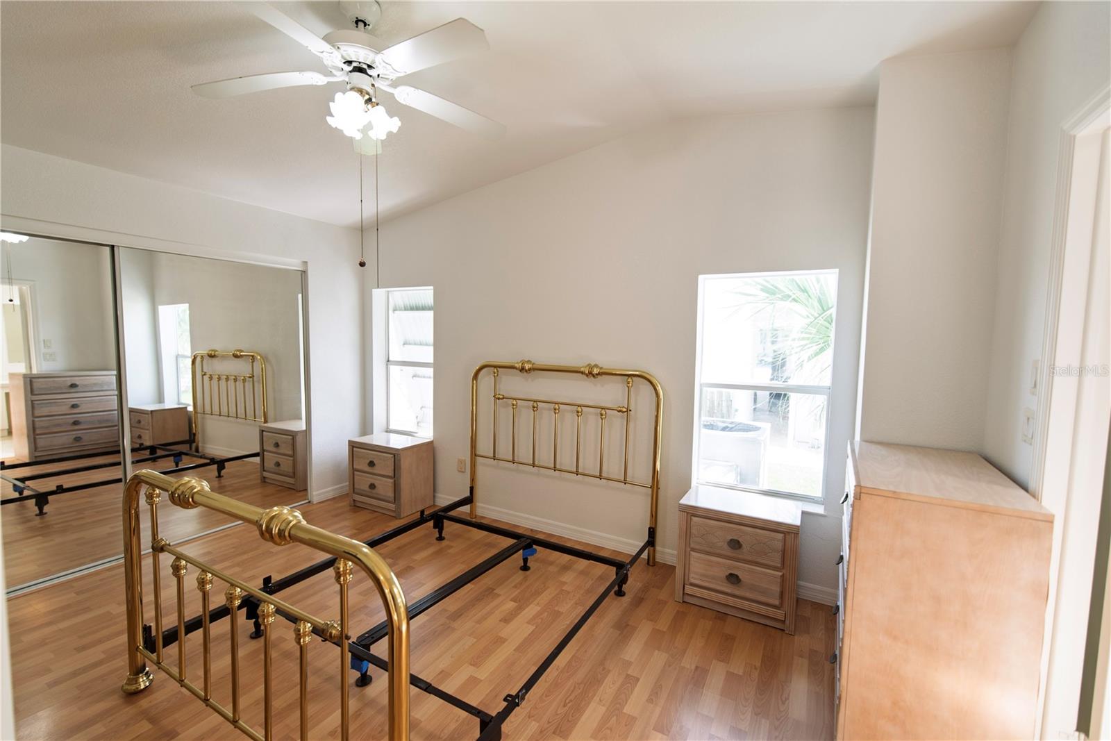 Bedroom with a brass bed frame, mirrored closet doors, and light wood dressers.