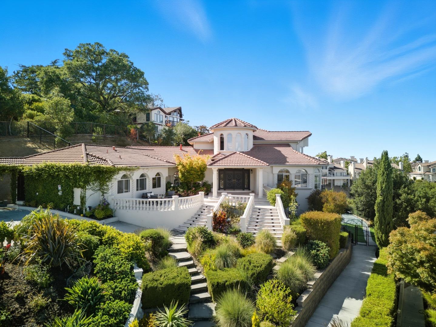White two-story home with terracotta tile roofs, broad entry stairs, and landscaped front gardens.