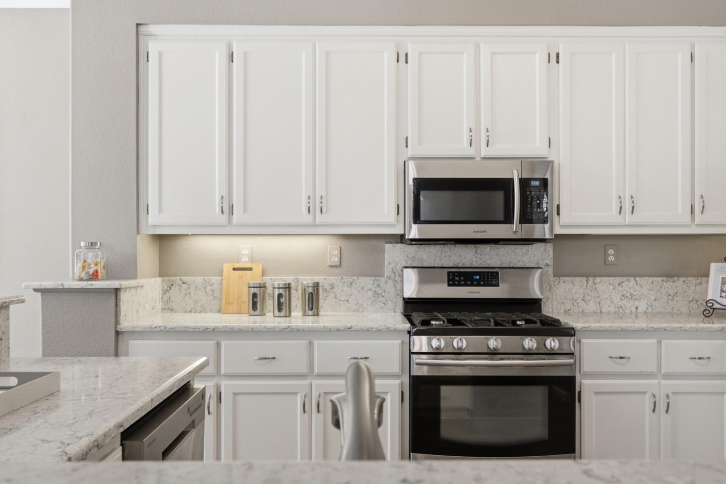 Kitchen with white cabinets, stone counters, and stainless steel gas range and microwave.