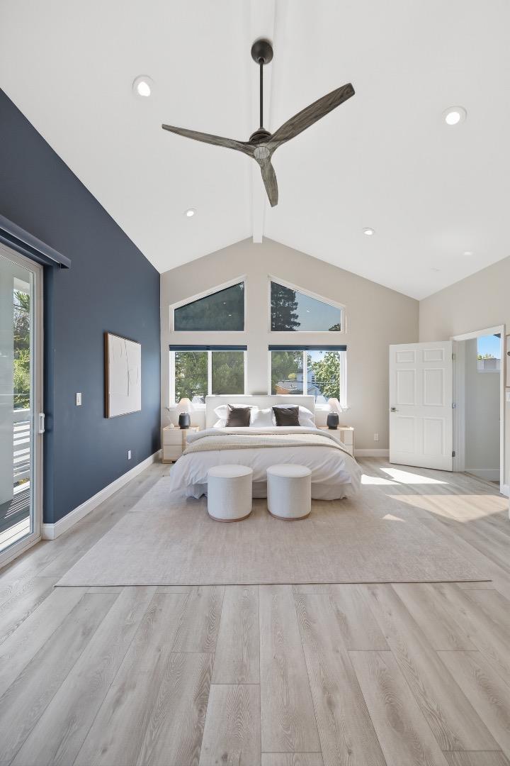 Staged bedroom with a vaulted ceiling, large ceiling fan, and high triangular windows above the bed.