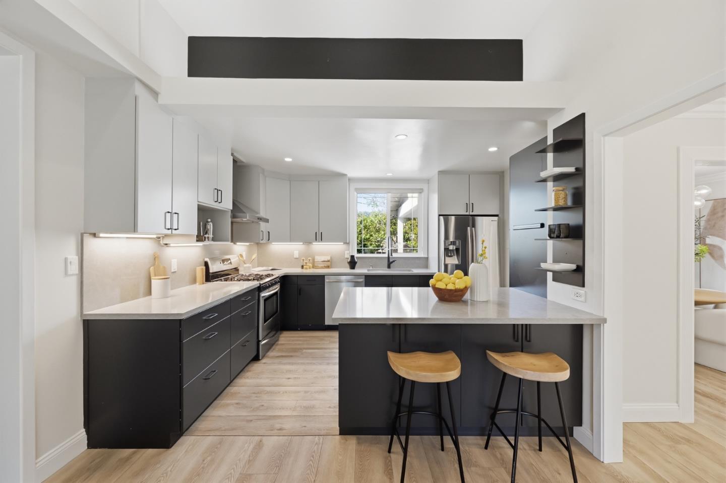 Modern kitchen with dark cabinetry, white counters, a large island, and two wooden stools.